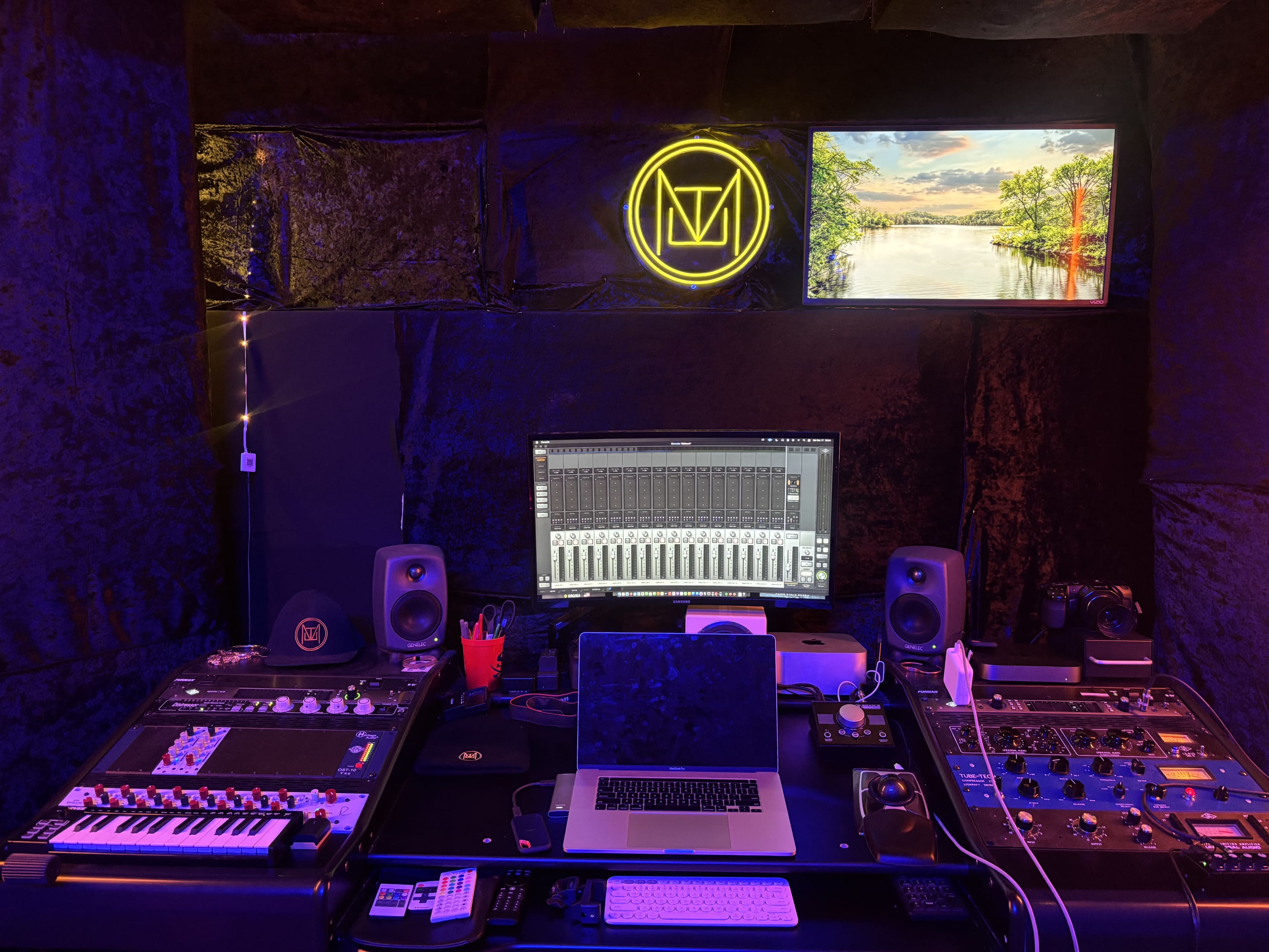 The image shows a recording studio with various audio equipment, including a computer, mixing console, and speakers, illuminated by a neon sign and ambient lighting.