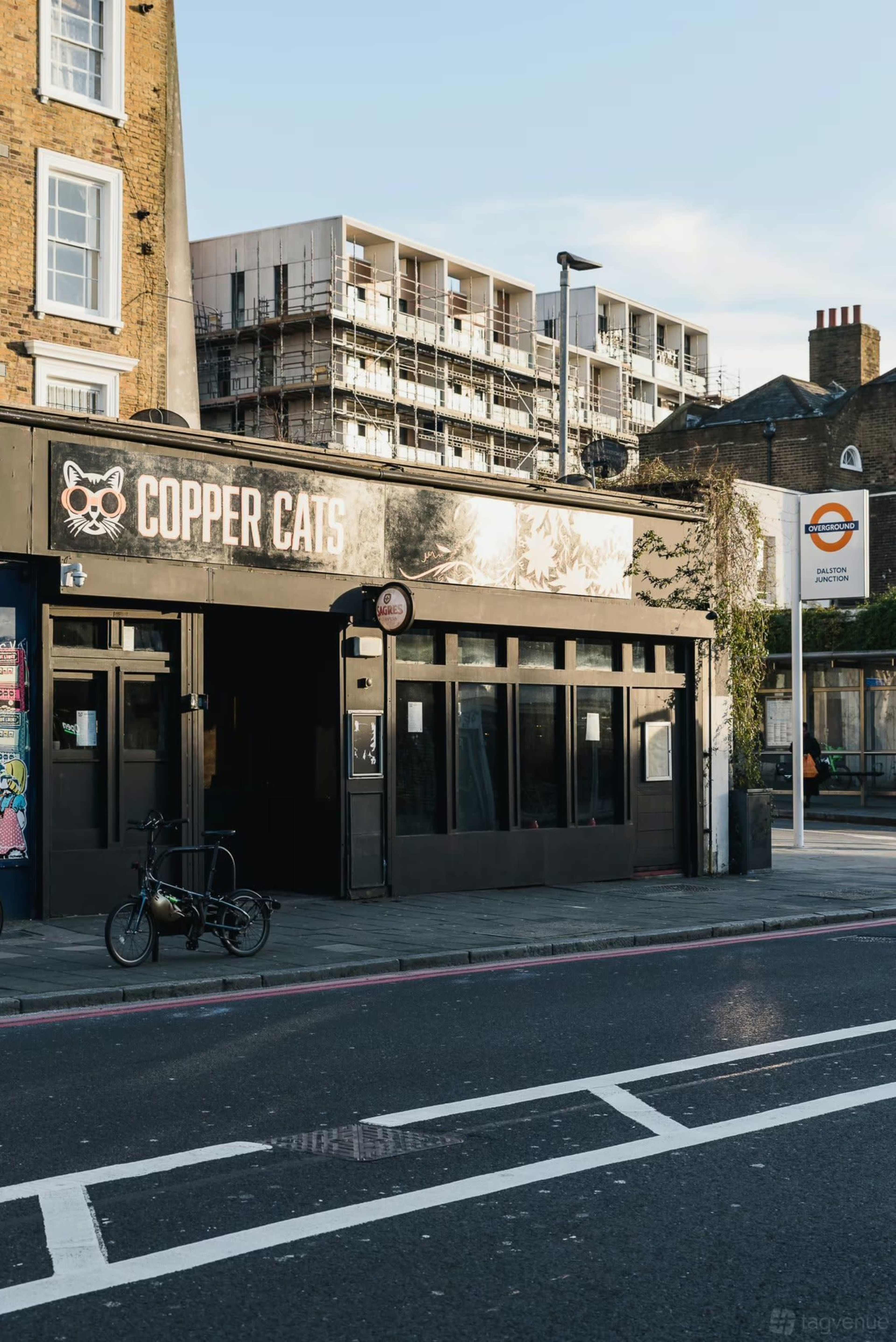 The image shows a street view of a building with a sign that reads "Copper Cats," located next to a construction site with scaffolding and modern apartment buildings in the background.