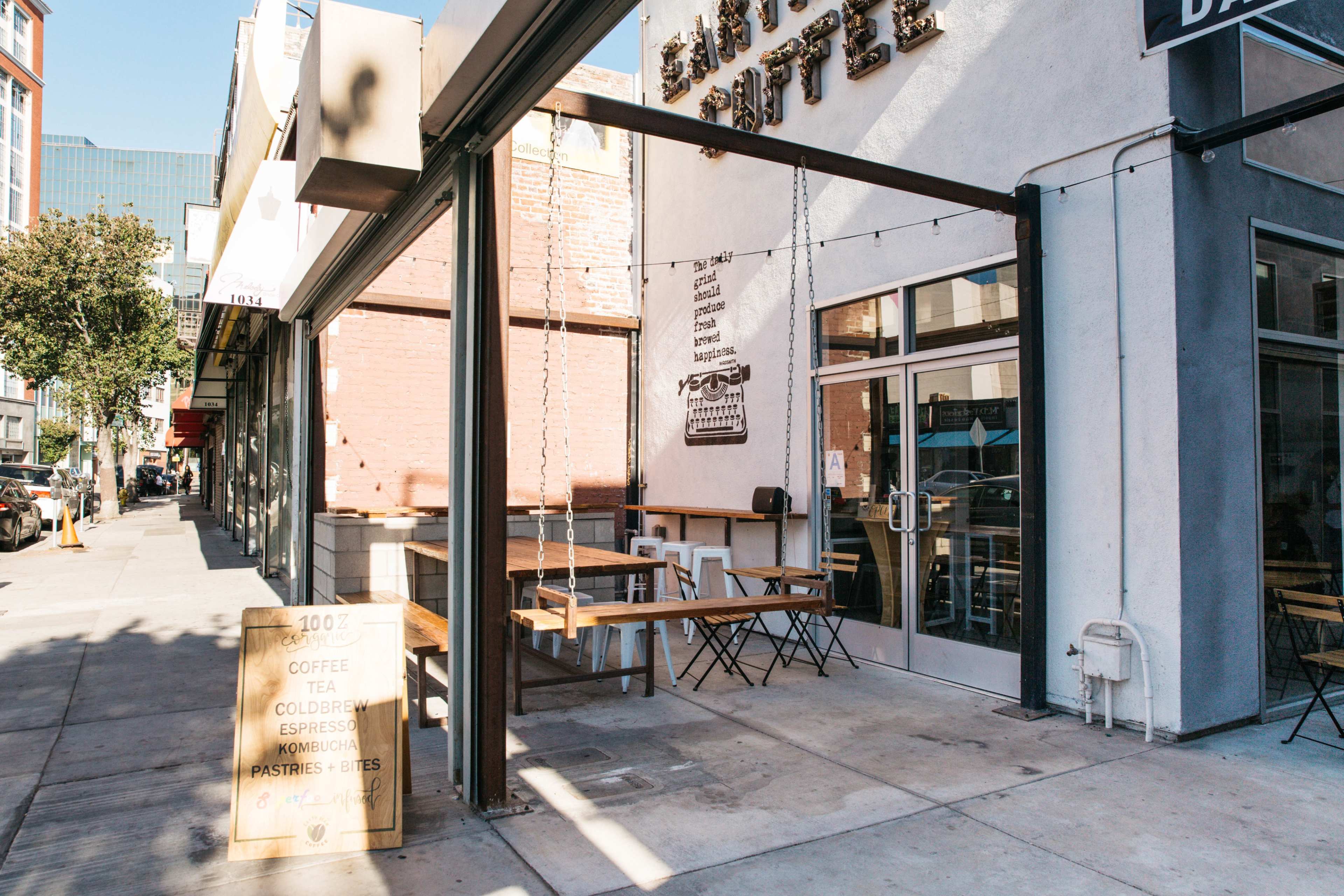 A coffee shop with outdoor seating and a sign displaying menu items is located on a sidewalk in a city.