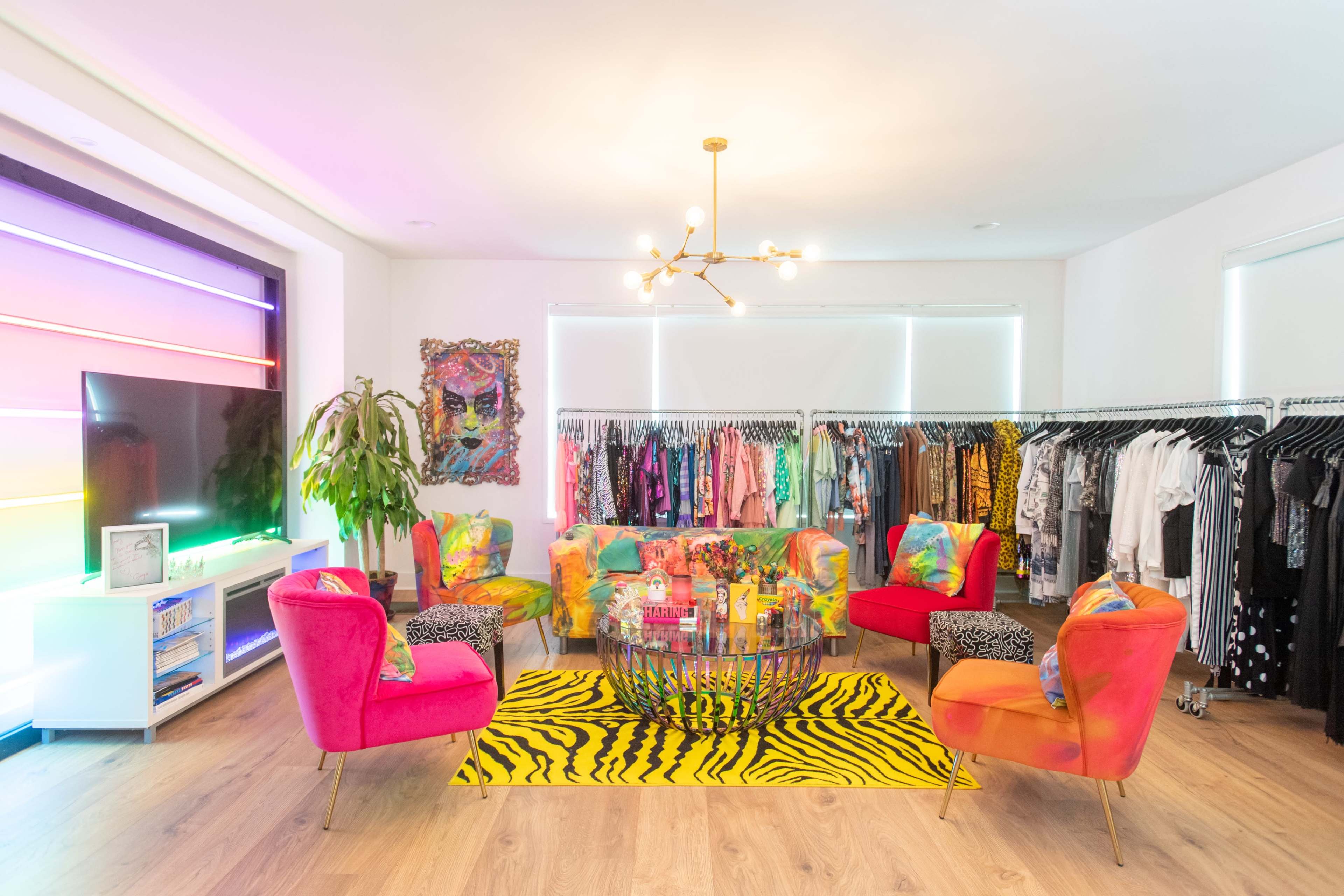 A vibrant boutique features colorful seating and a zebra-striped rug surrounded by racks of clothing.