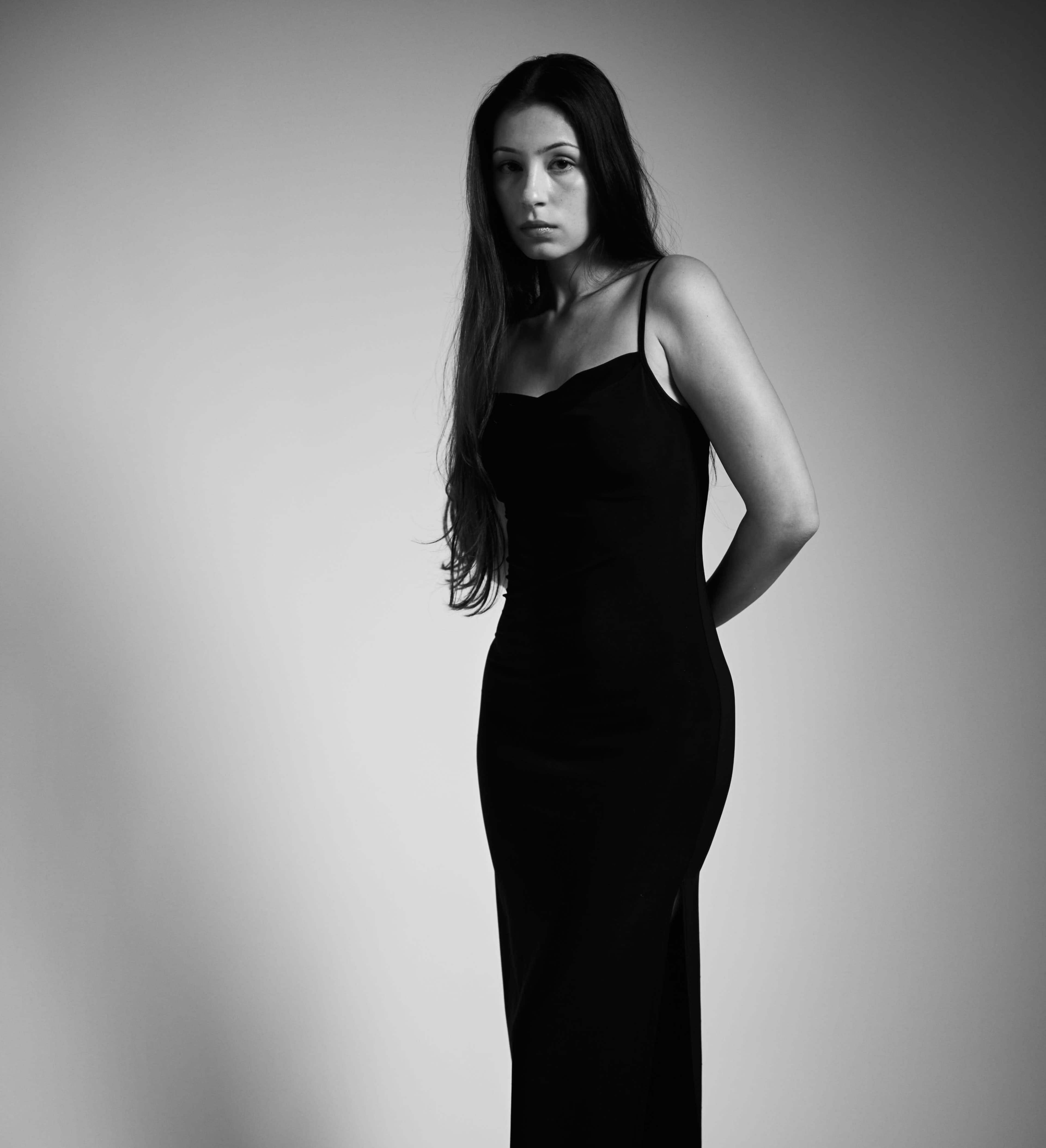 A woman wearing a black dress stands against a plain, light background.