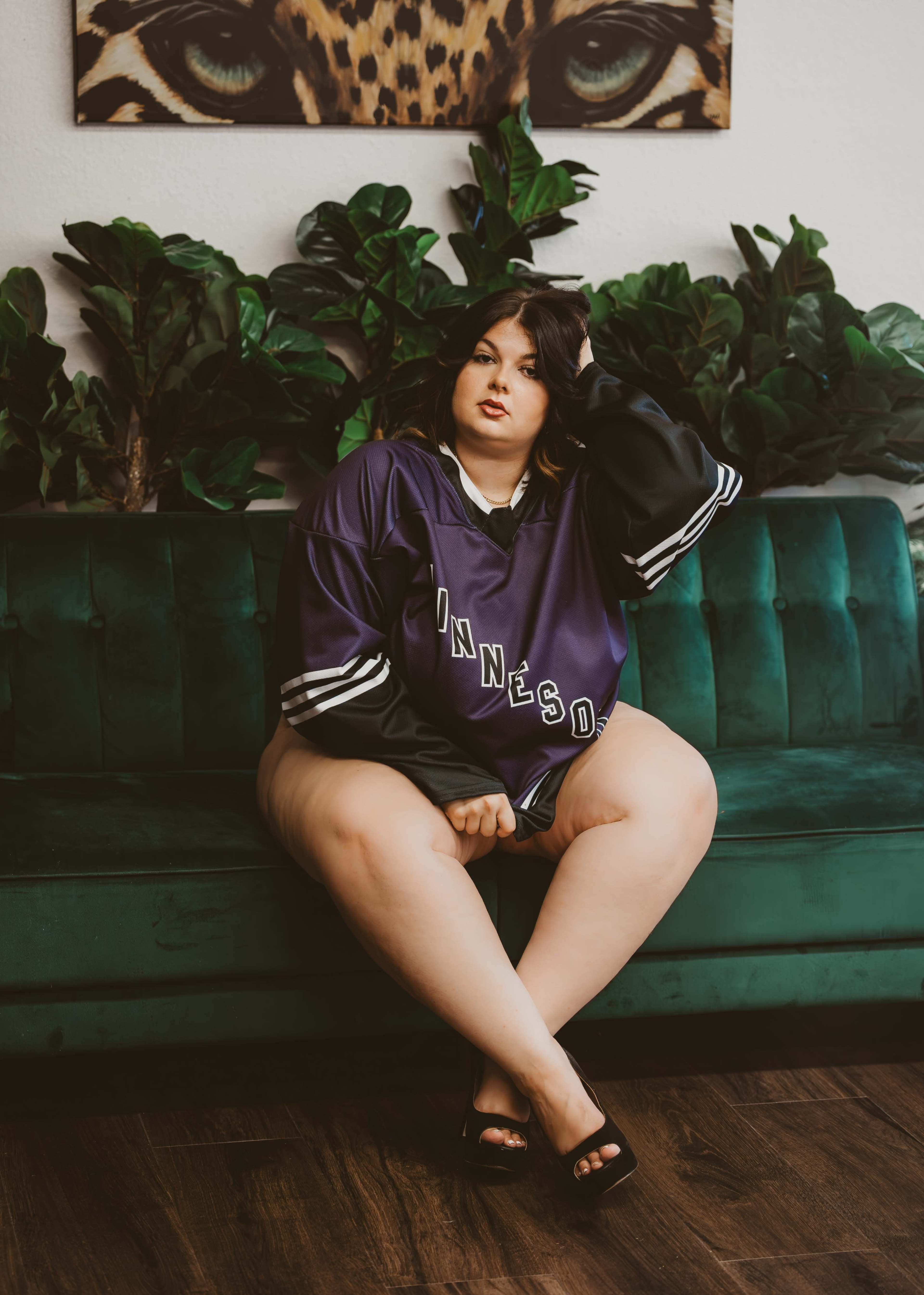 A person sits on a green couch, wearing a purple Minnesota shirt, with a decorative wall featuring a leopard print above.
