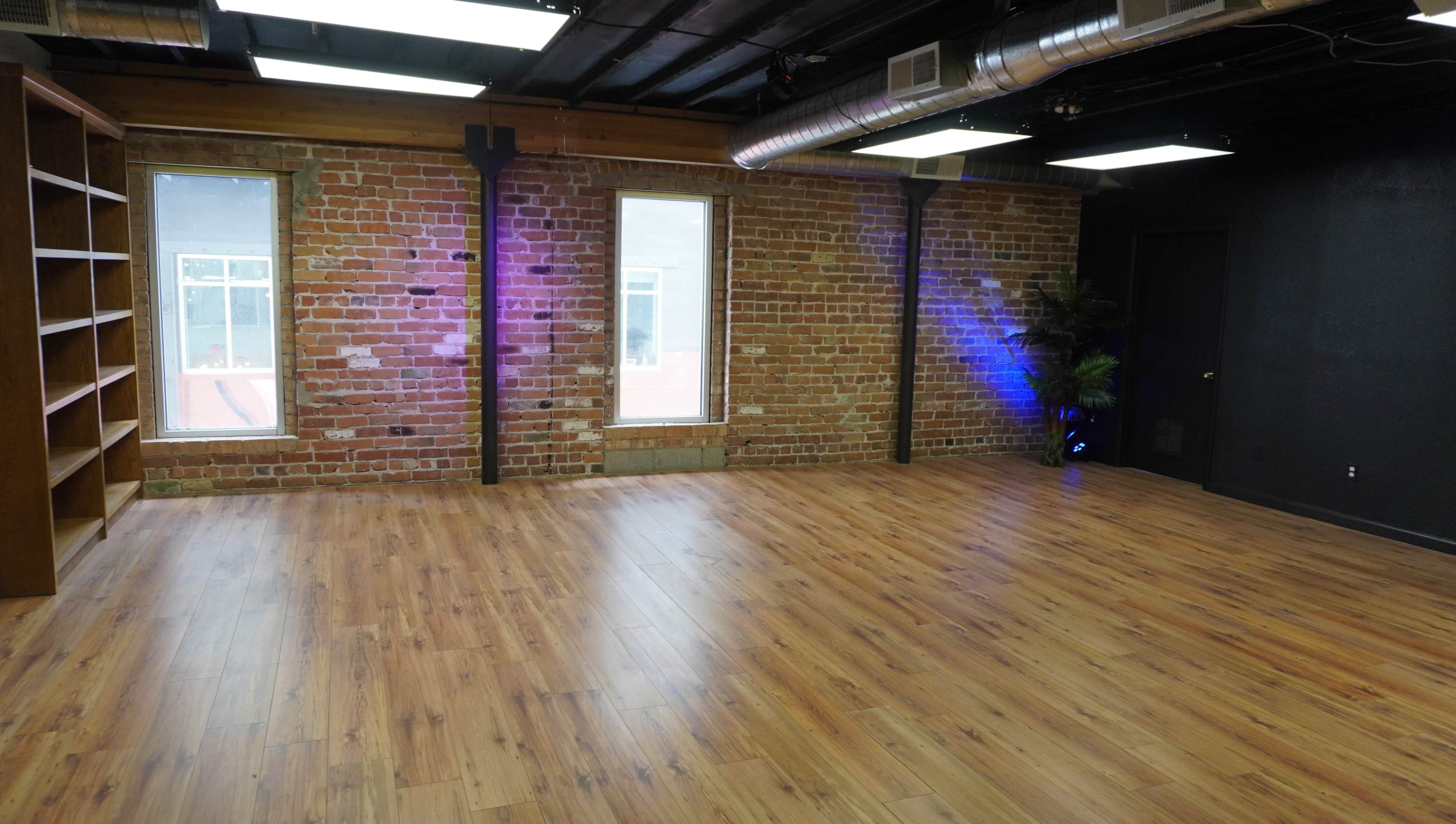 An empty warehouse-style room with exposed brick walls, large windows, and wooden flooring.
