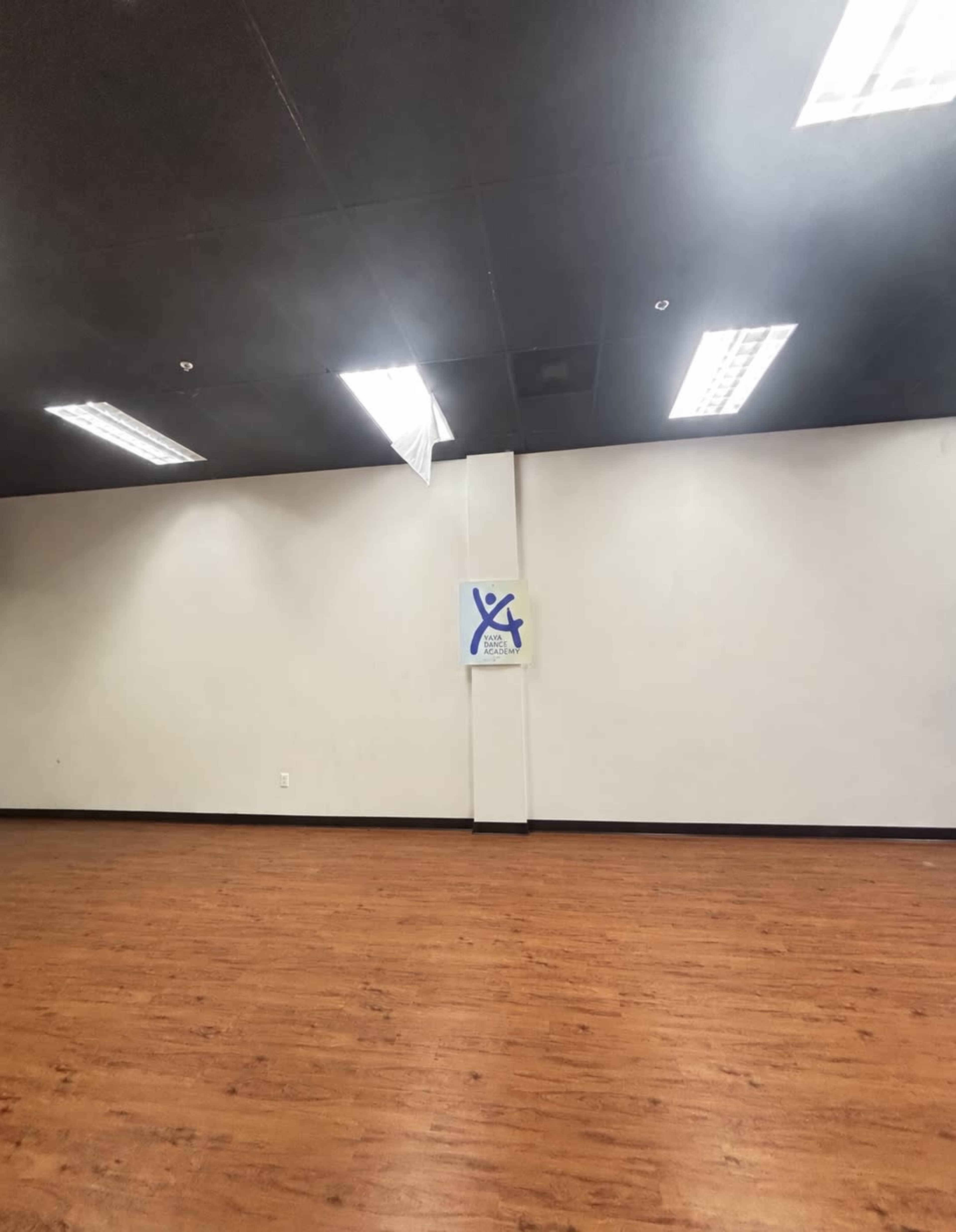 The image shows a spacious, empty room with wooden flooring and a sign on one of the walls.