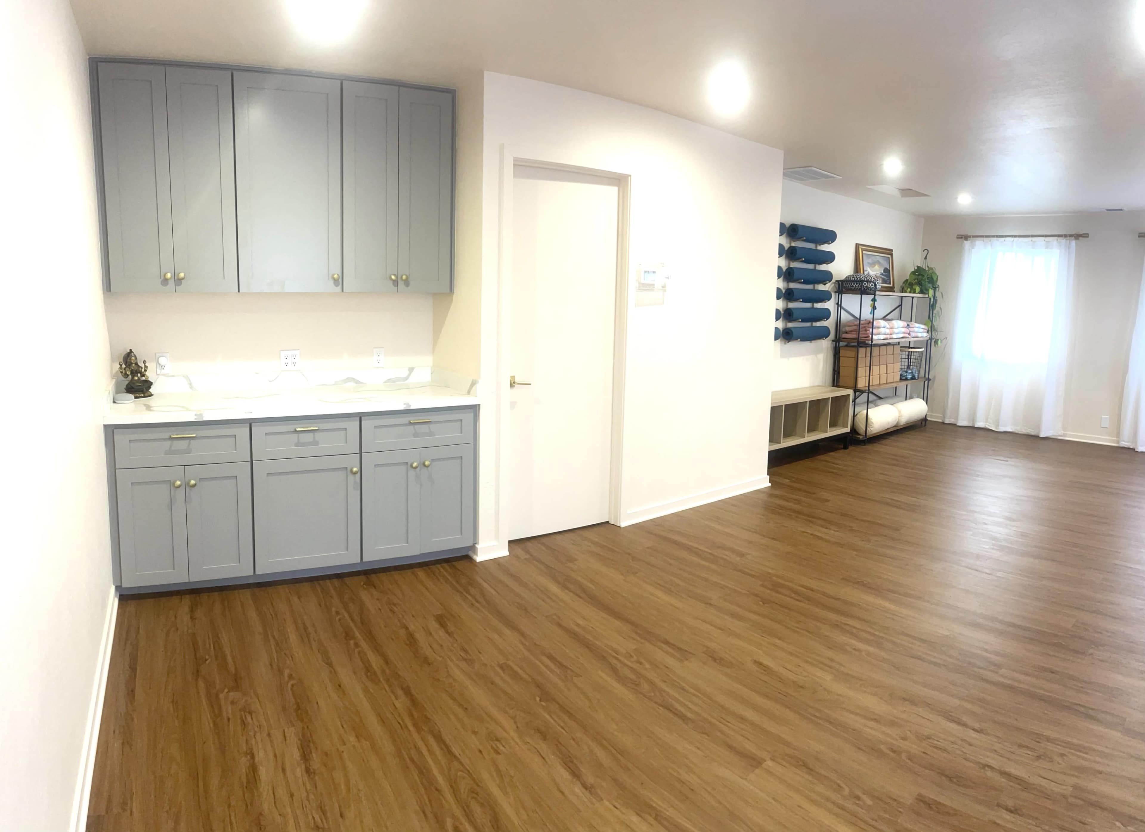 A spacious room with light-colored walls, a gray storage cabinet, a white door, and shelves stacked with rolled mats.