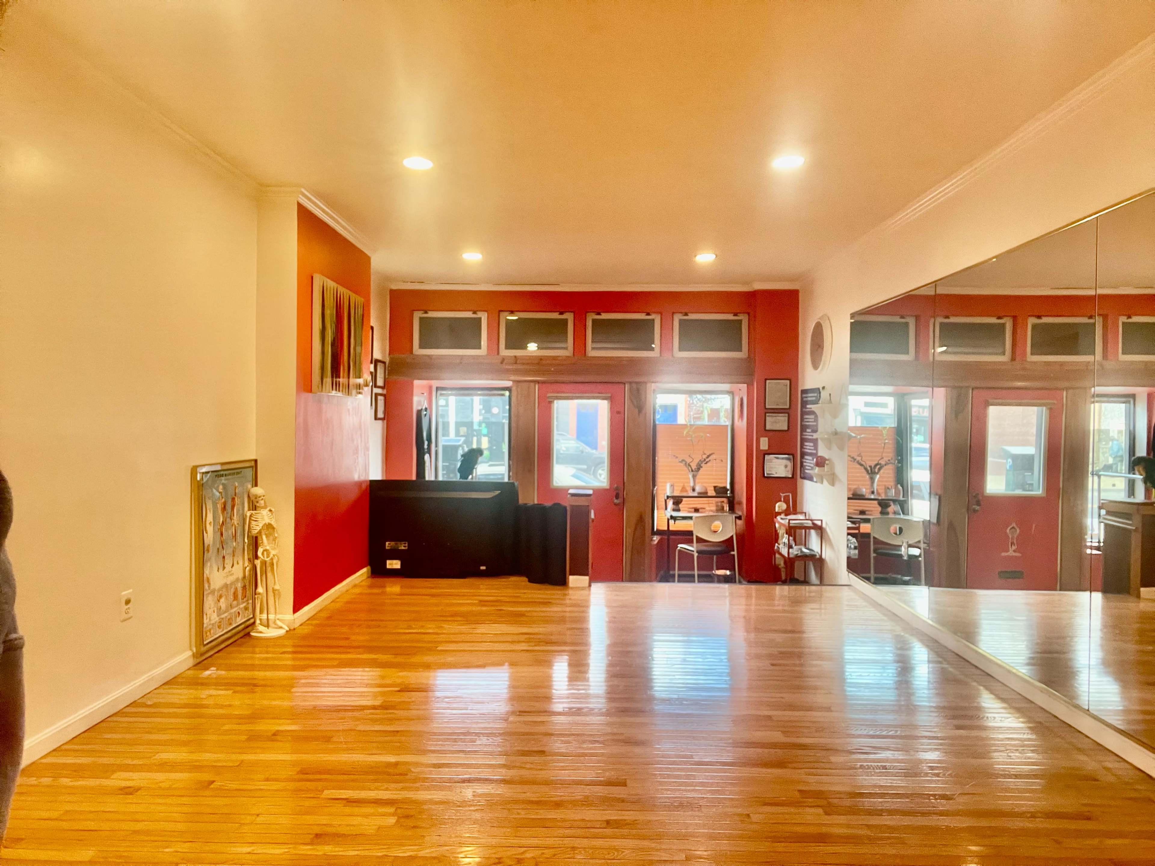 The image shows a spacious interior with wooden flooring, red walls, a large mirror, and two front doors leading outside.