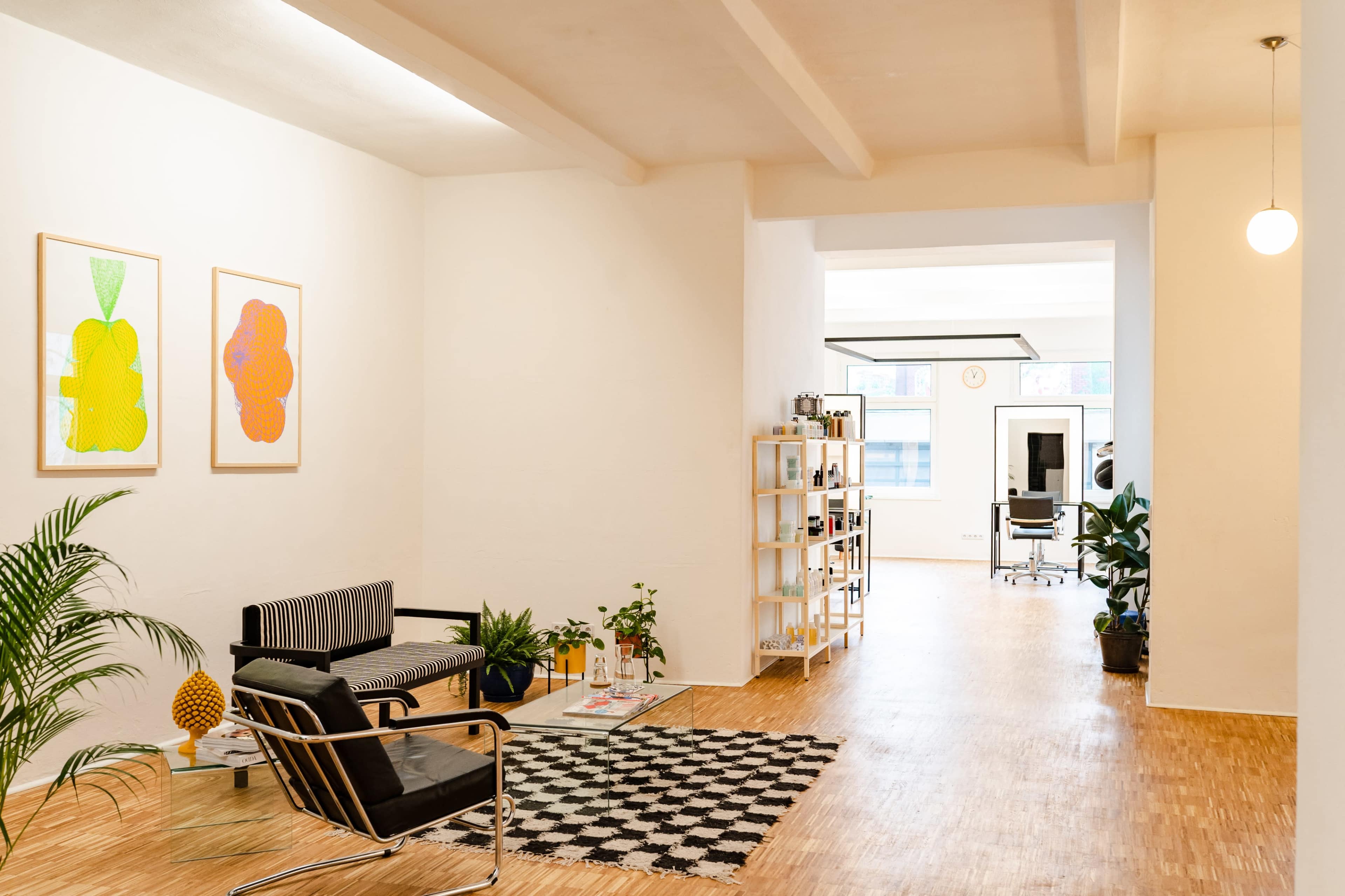 A spacious, modern office area with light wooden floors, plants, and a mix of seating and shelving arrangements.