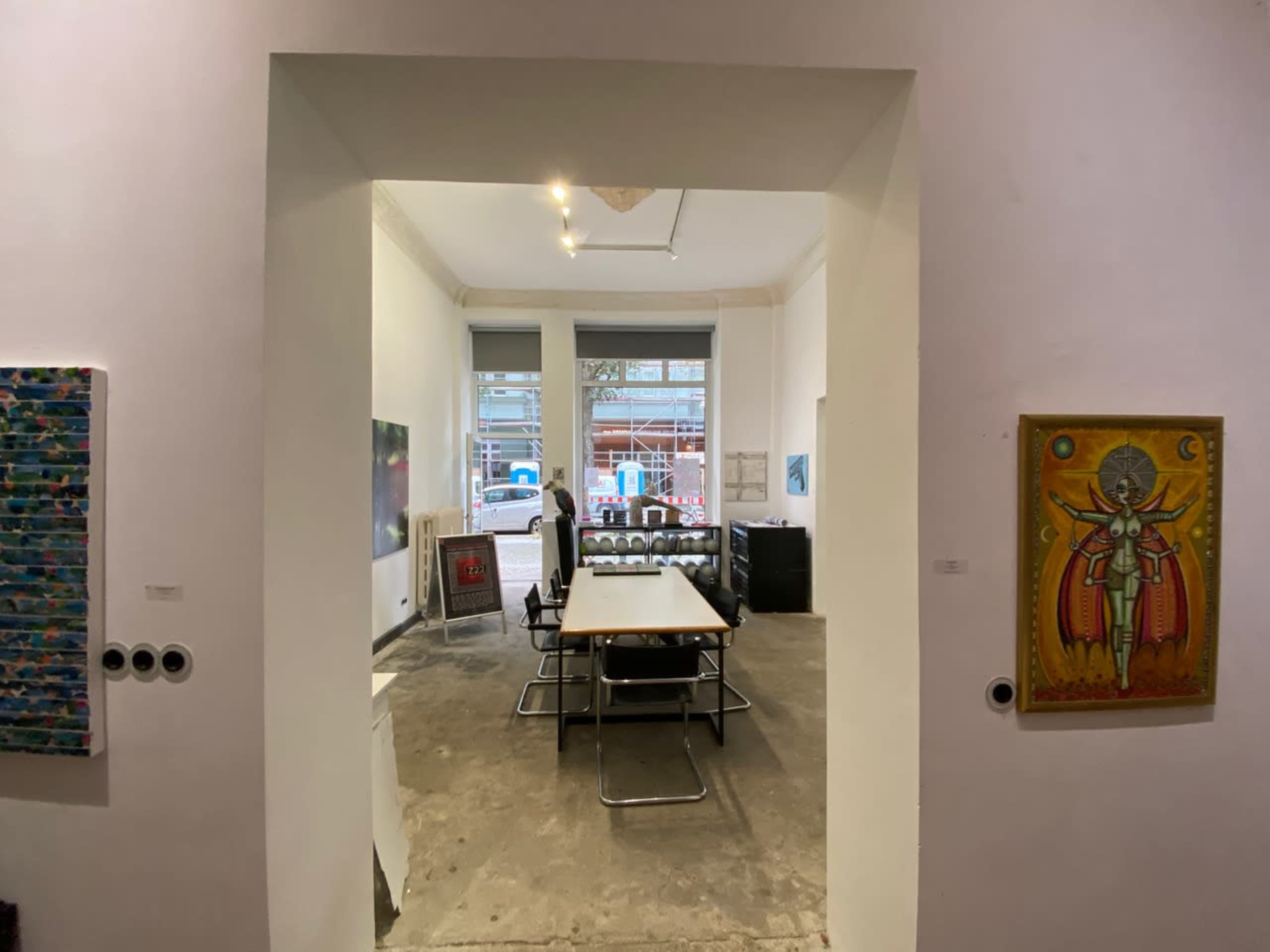 A modern, minimalistic meeting room with a large table surrounded by chairs, framed by an archway and artworks displayed on the walls.