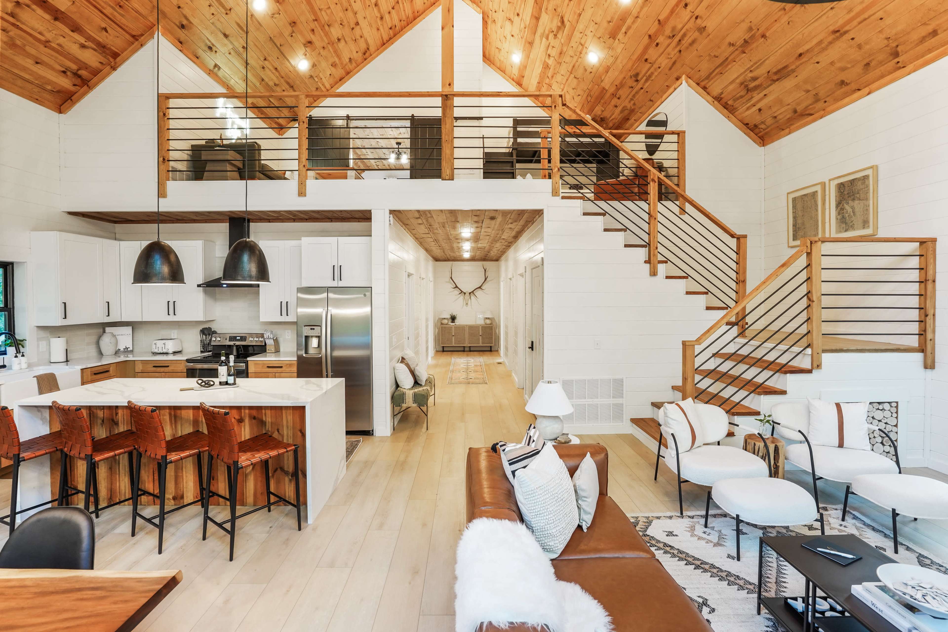 A spacious, modern interior of a cabin featuring a lofted area, open kitchen, and living space with a staircase and large windows.