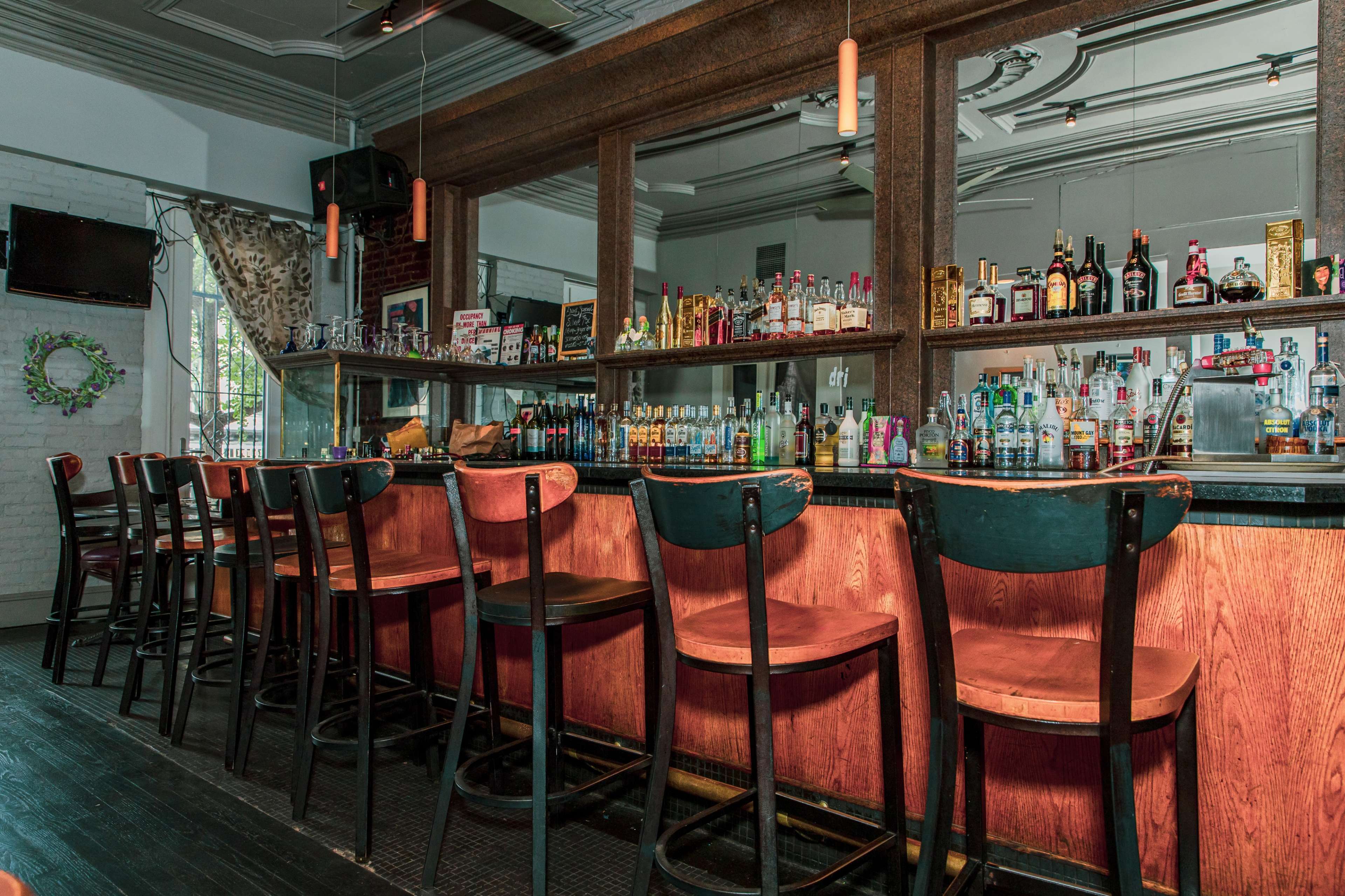A well-lit bar with wooden stools lined up in front of a counter filled with various bottles of liquor.