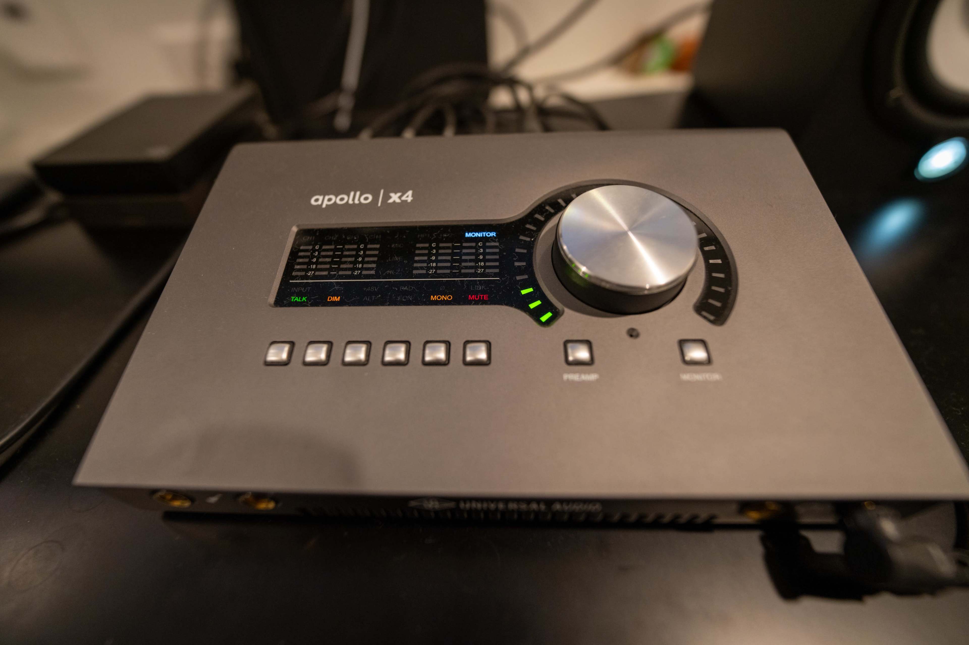 The image shows an Apollo x4 audio interface with a large central knob and various buttons on its surface, positioned on a tabletop.