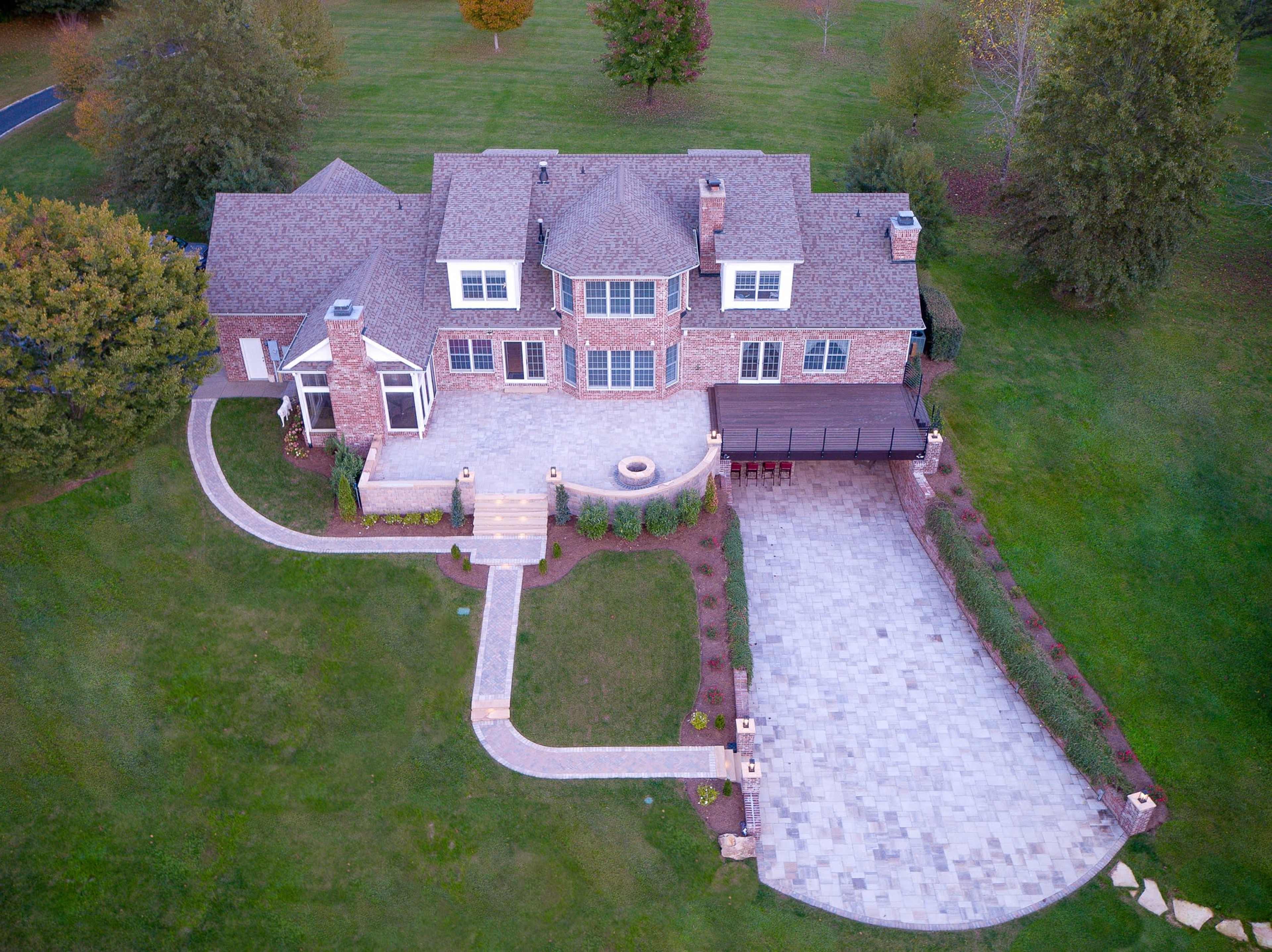 An aerial view shows a large brick house with a landscaped yard, stone pathway, and a patio area in front.