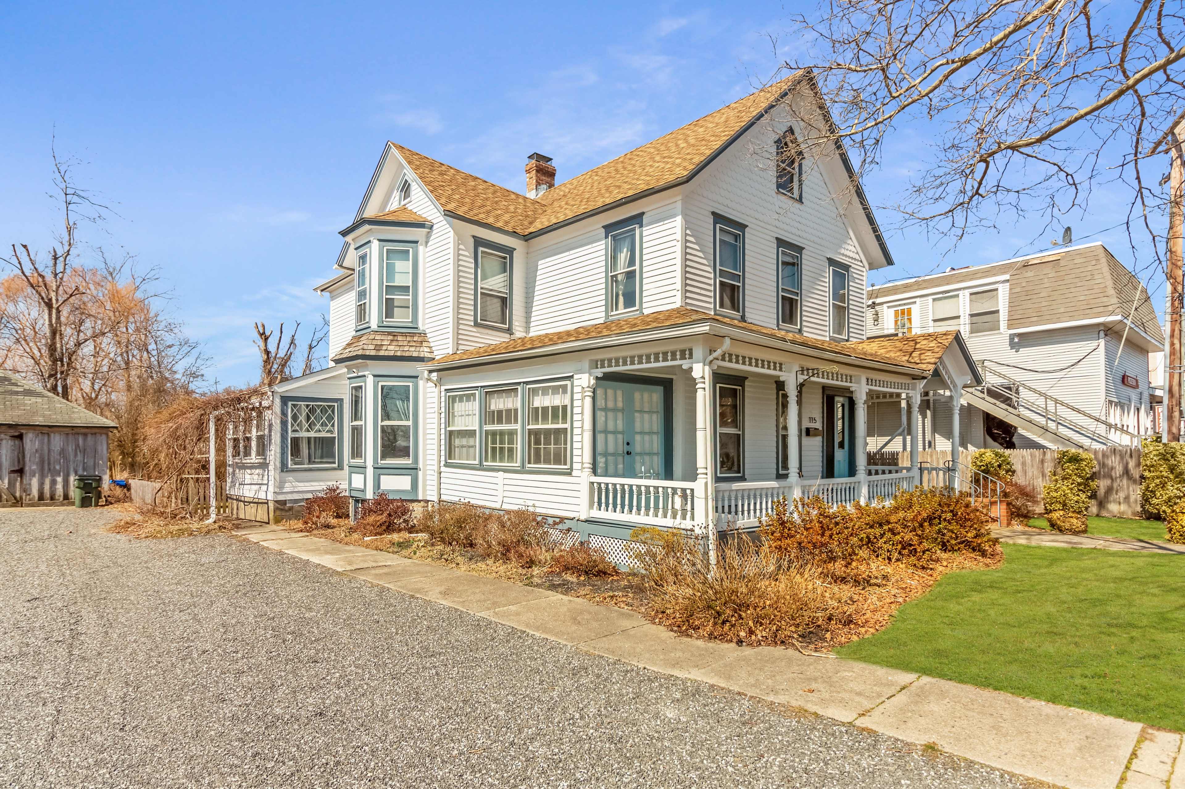 A large, white Victorian-style house with a wraparound porch and a gravel pathway leading to it.