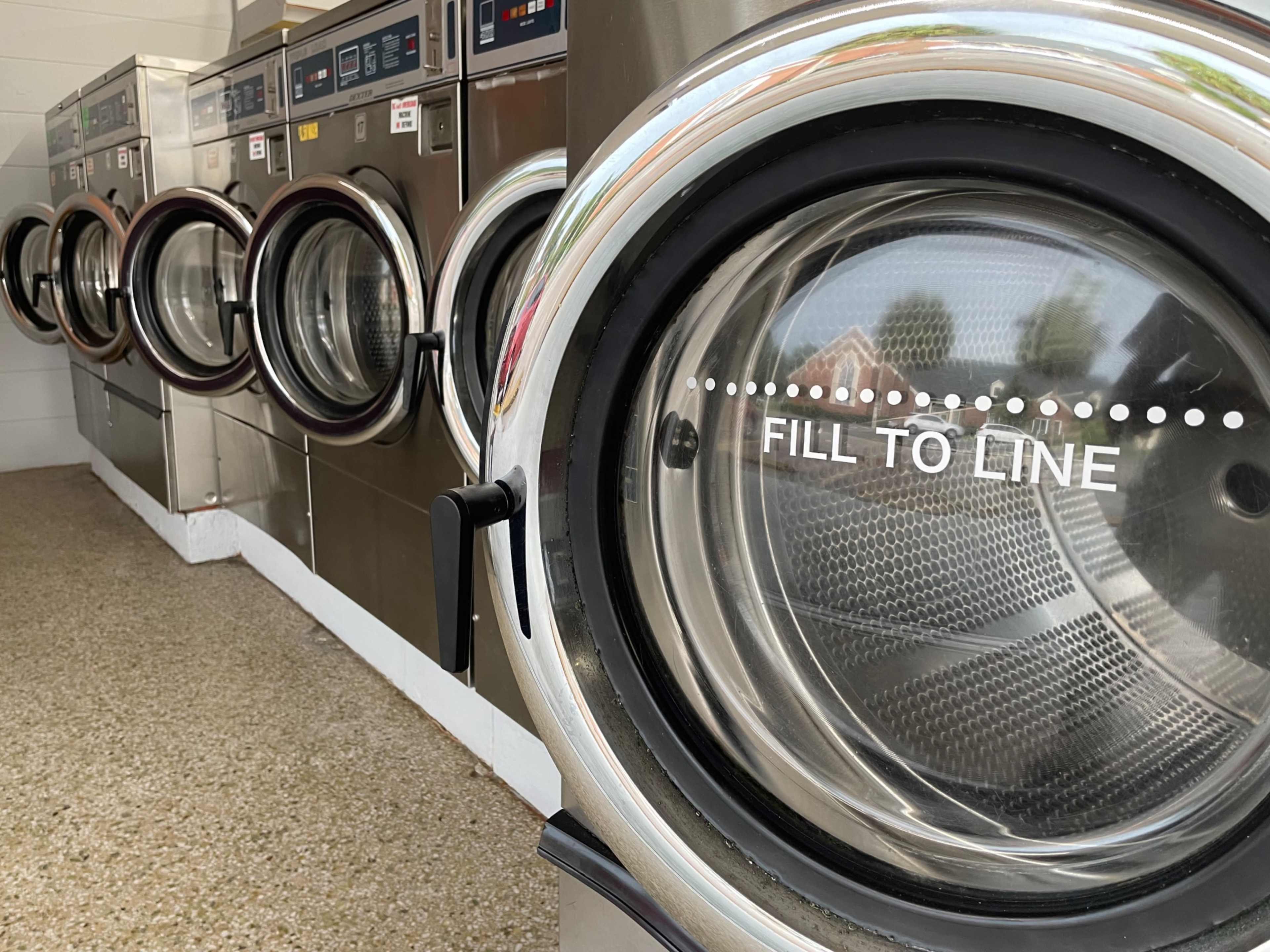 A row of washing machines with clear glass doors displaying a "FILL TO LINE" indicator.