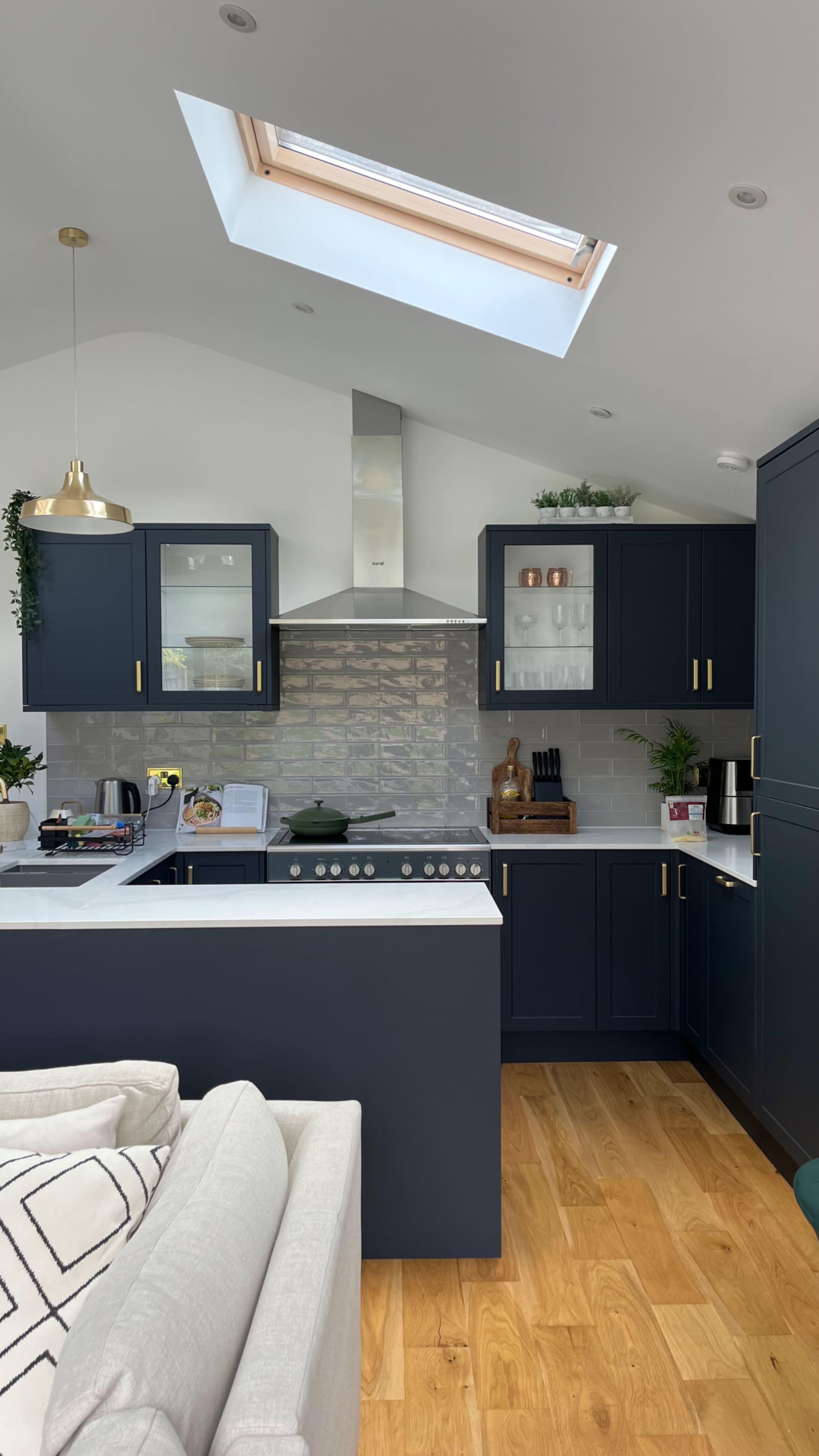 The kitchen features dark blue cabinetry, a stainless steel range hood, and wooden flooring, with a skylight providing natural light.