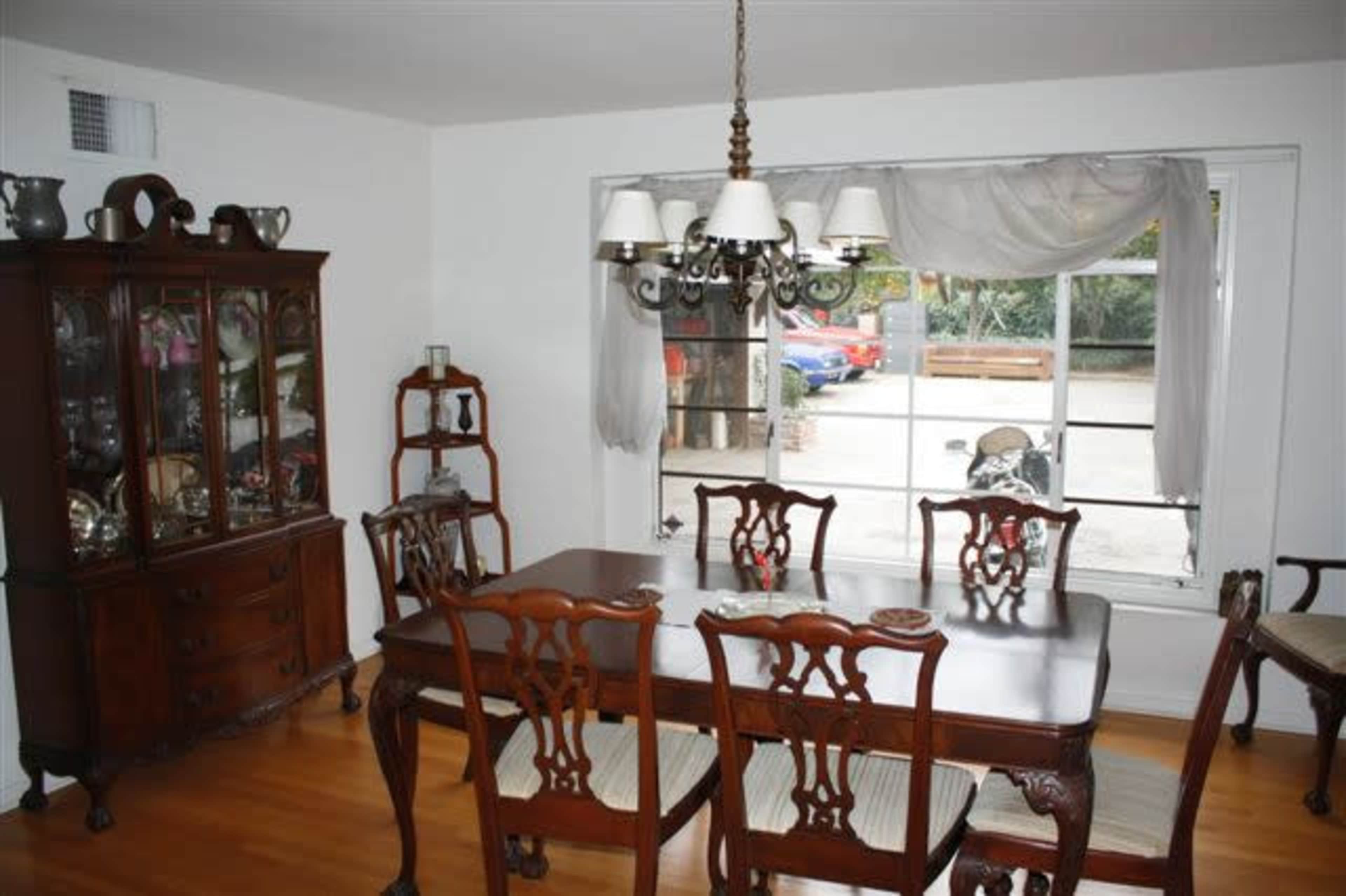 A dining room featuring a wooden table with chairs, a china cabinet filled with dishes, and a large window overlooking an outdoor area.