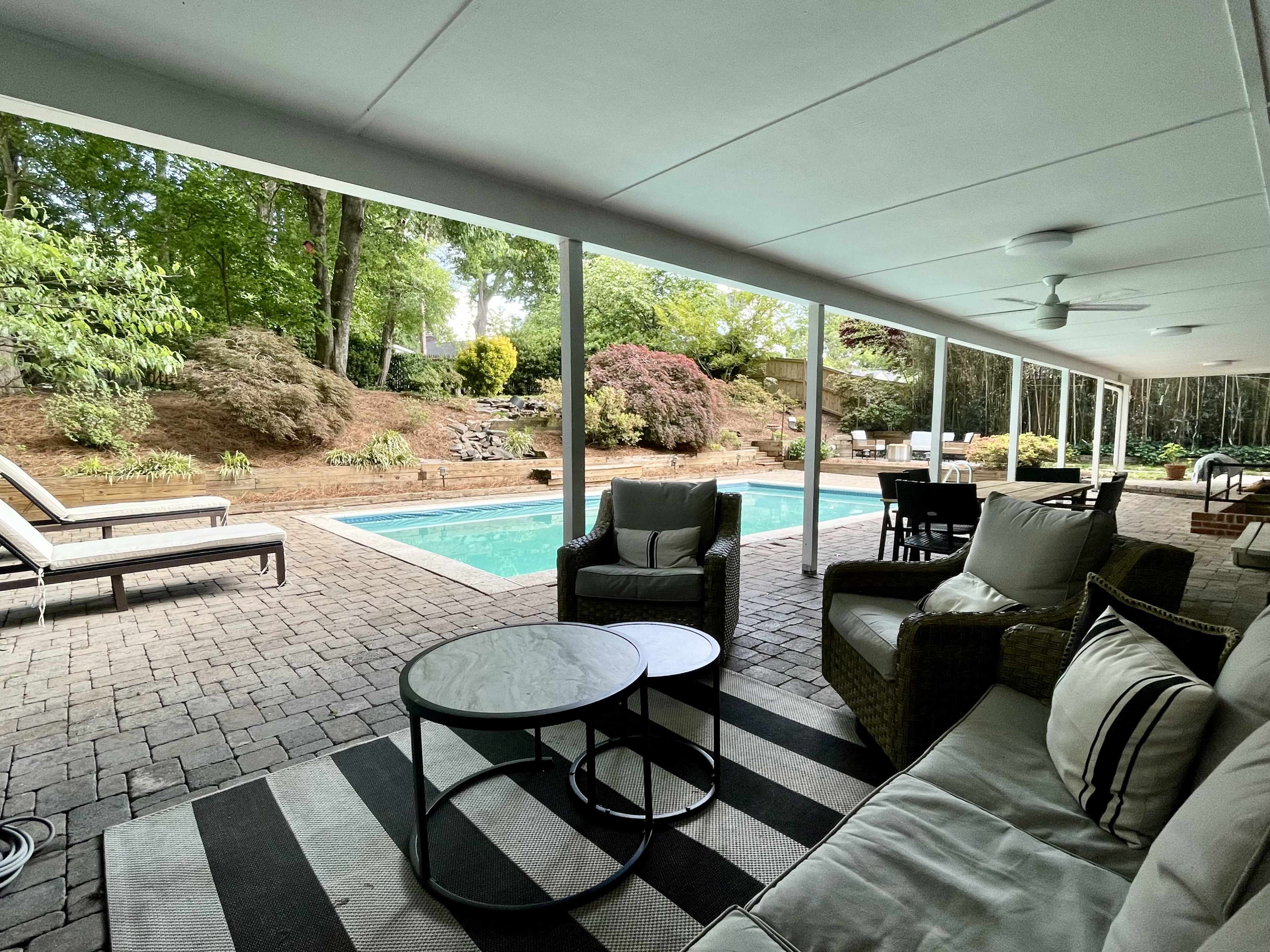 A covered patio area with seating and a view of a pool surrounded by landscaped greenery.