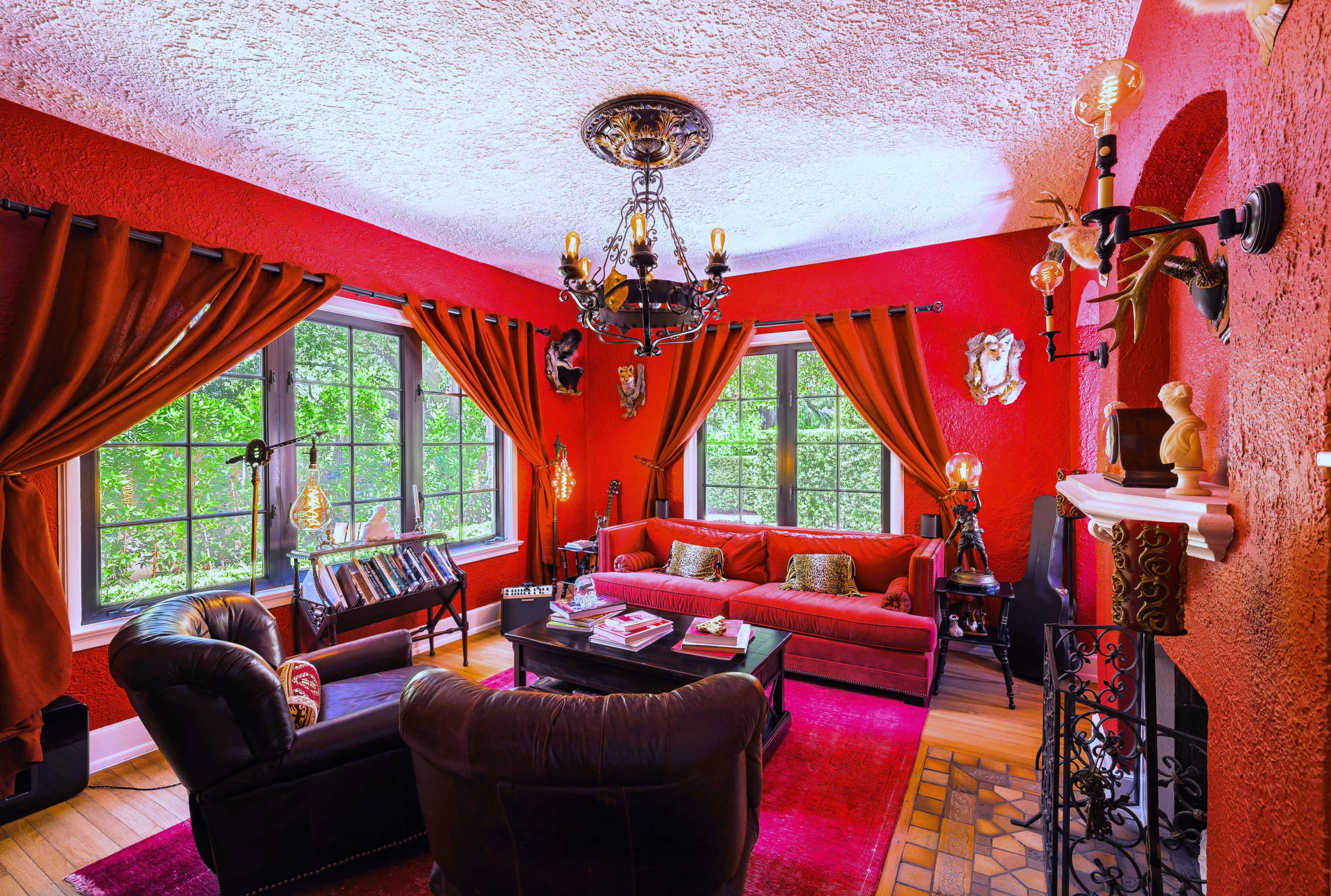 The image depicts a cozy living room featuring red walls, dark furniture, and large windows that let in natural light.