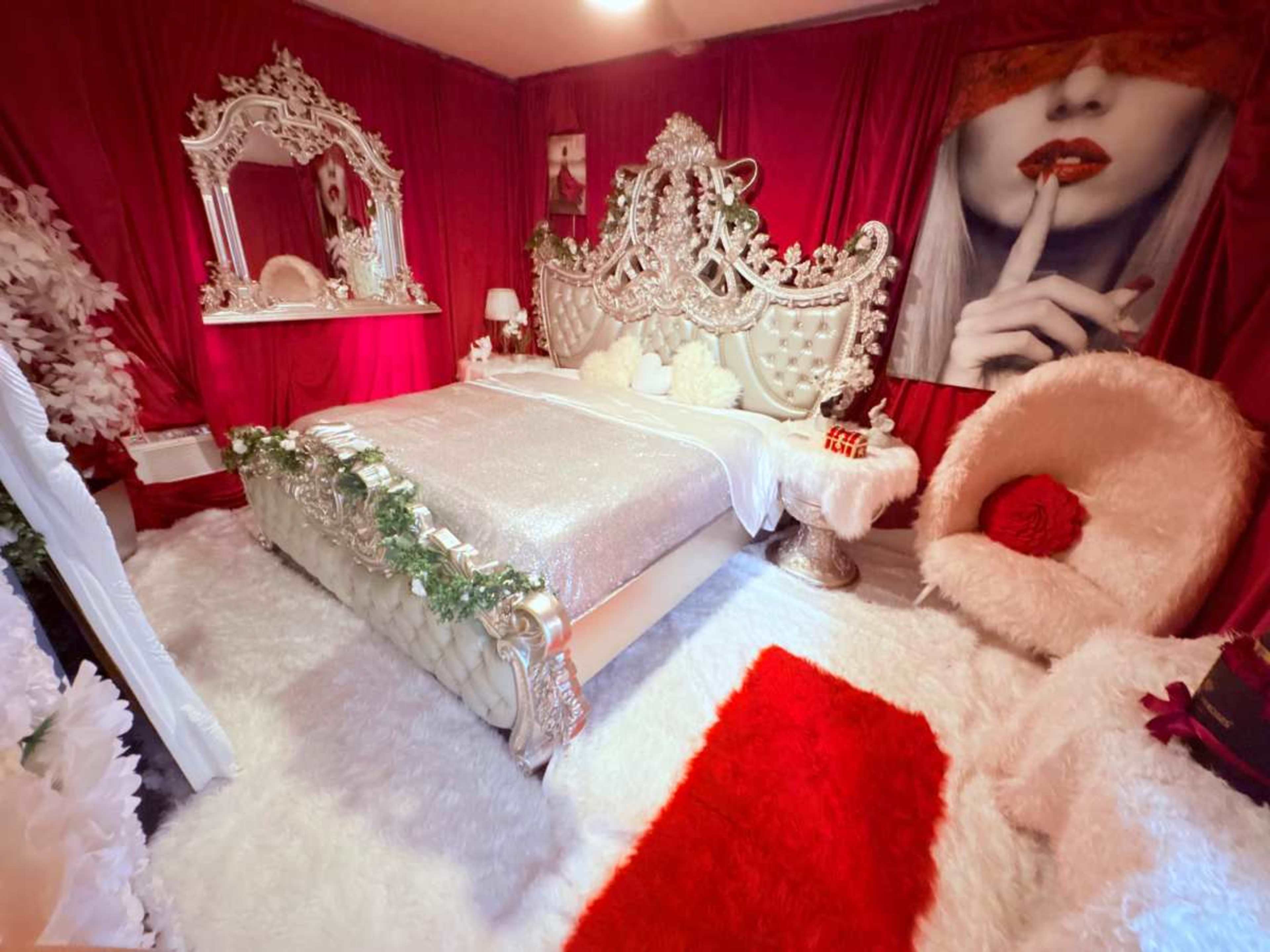 The image shows a lavish bedroom adorned with red and white decor, featuring a sparkling bed, plush rug, and elegant furnishings.