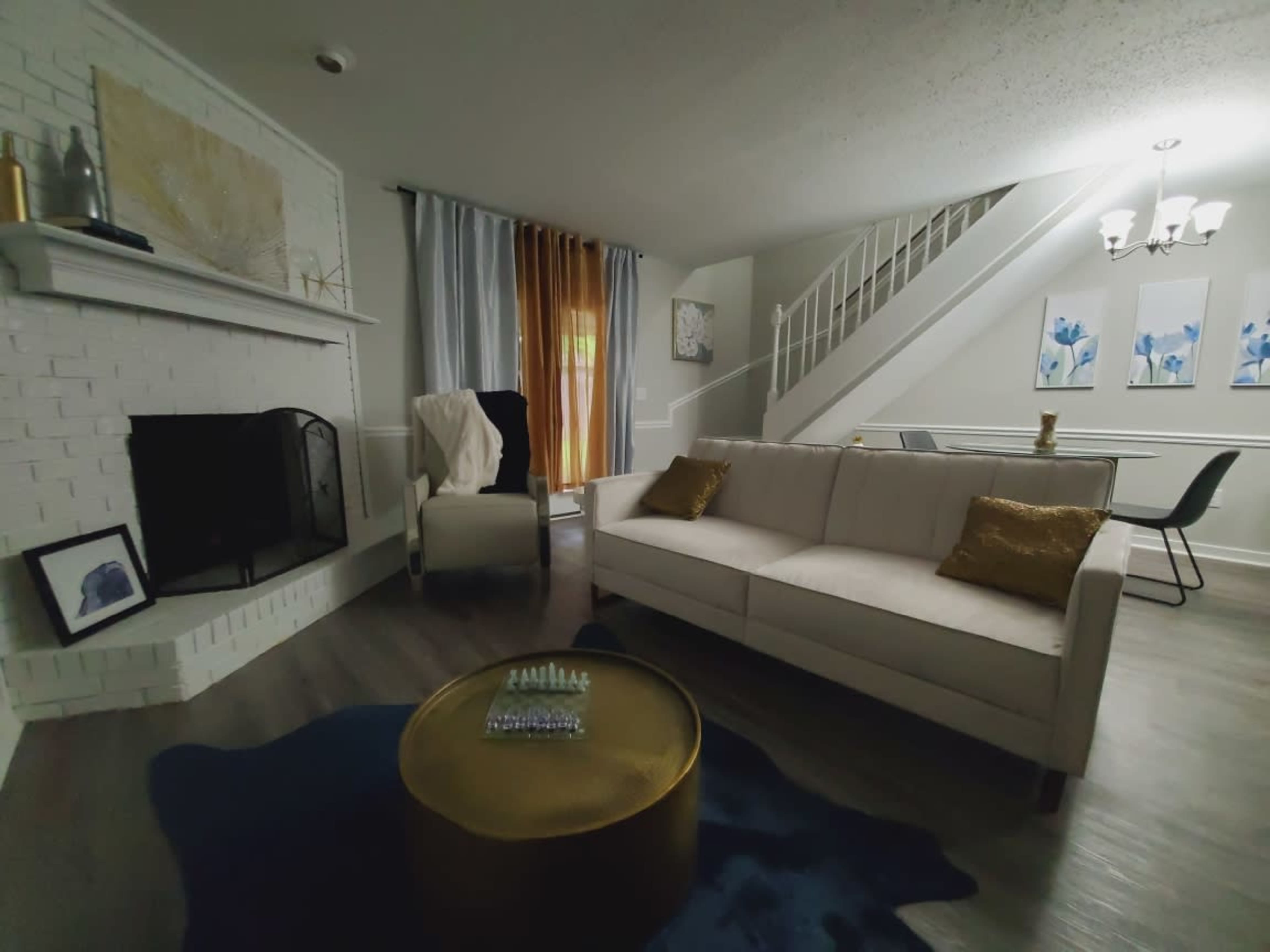 A modern living room with a white couch, a decorative gold coffee table, a fireplace, and a staircase in the background.