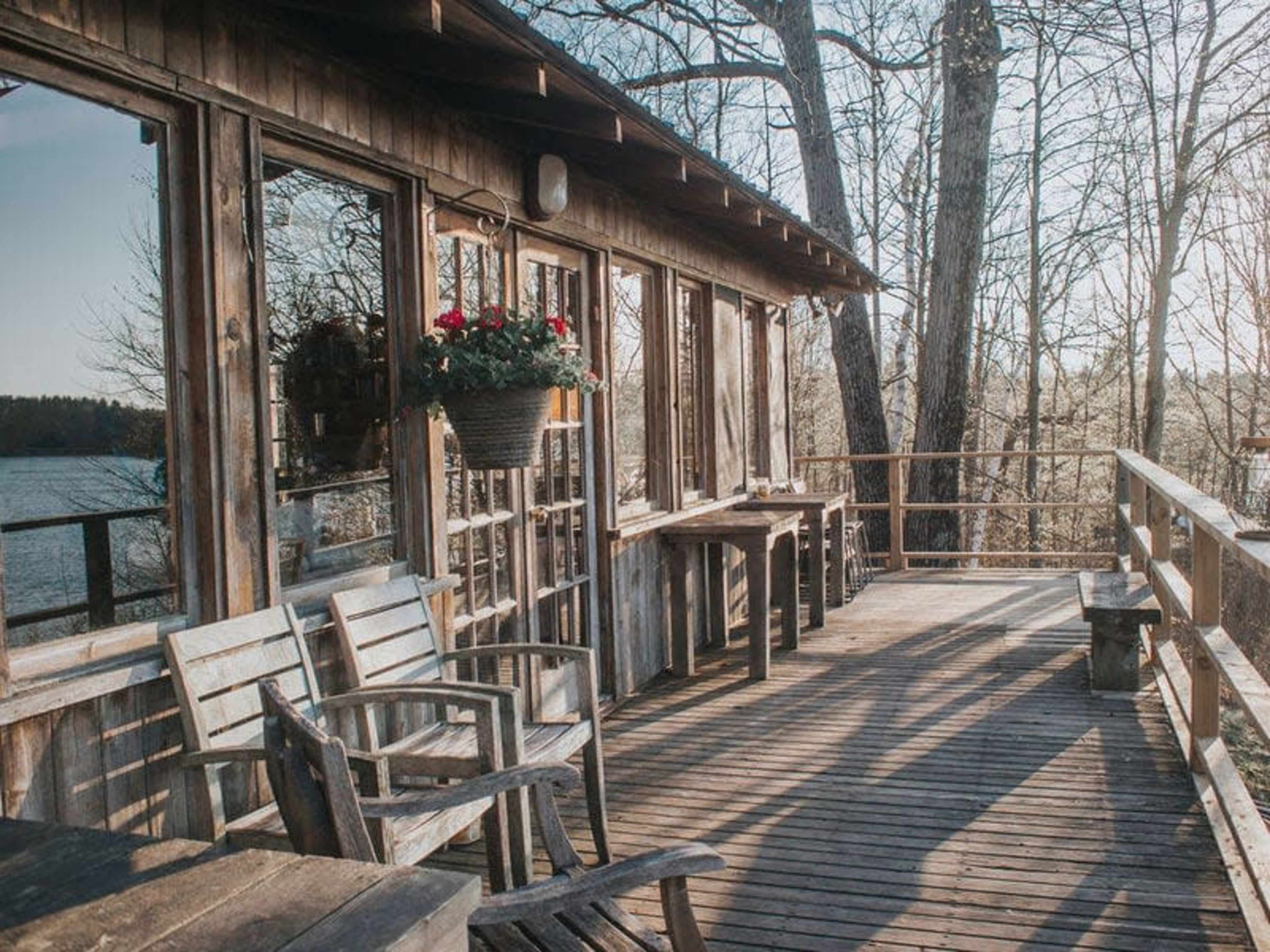 A wooden deck with several chairs and tables overlooks a body of water, framed by trees.