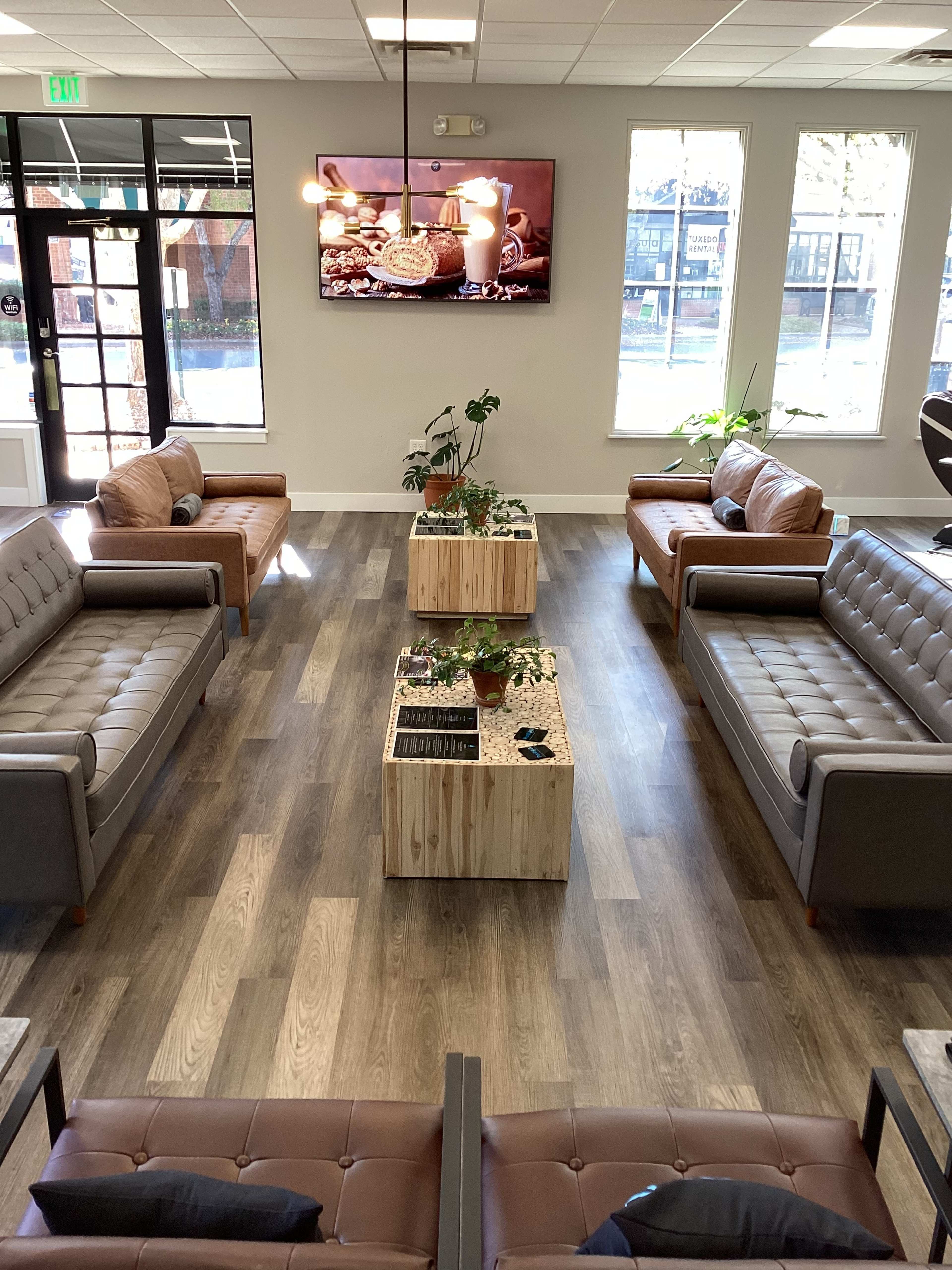 A modern lounge area with two sets of sofas facing each other and a wooden coffee table in the center, all under a television displaying a food-themed video.
