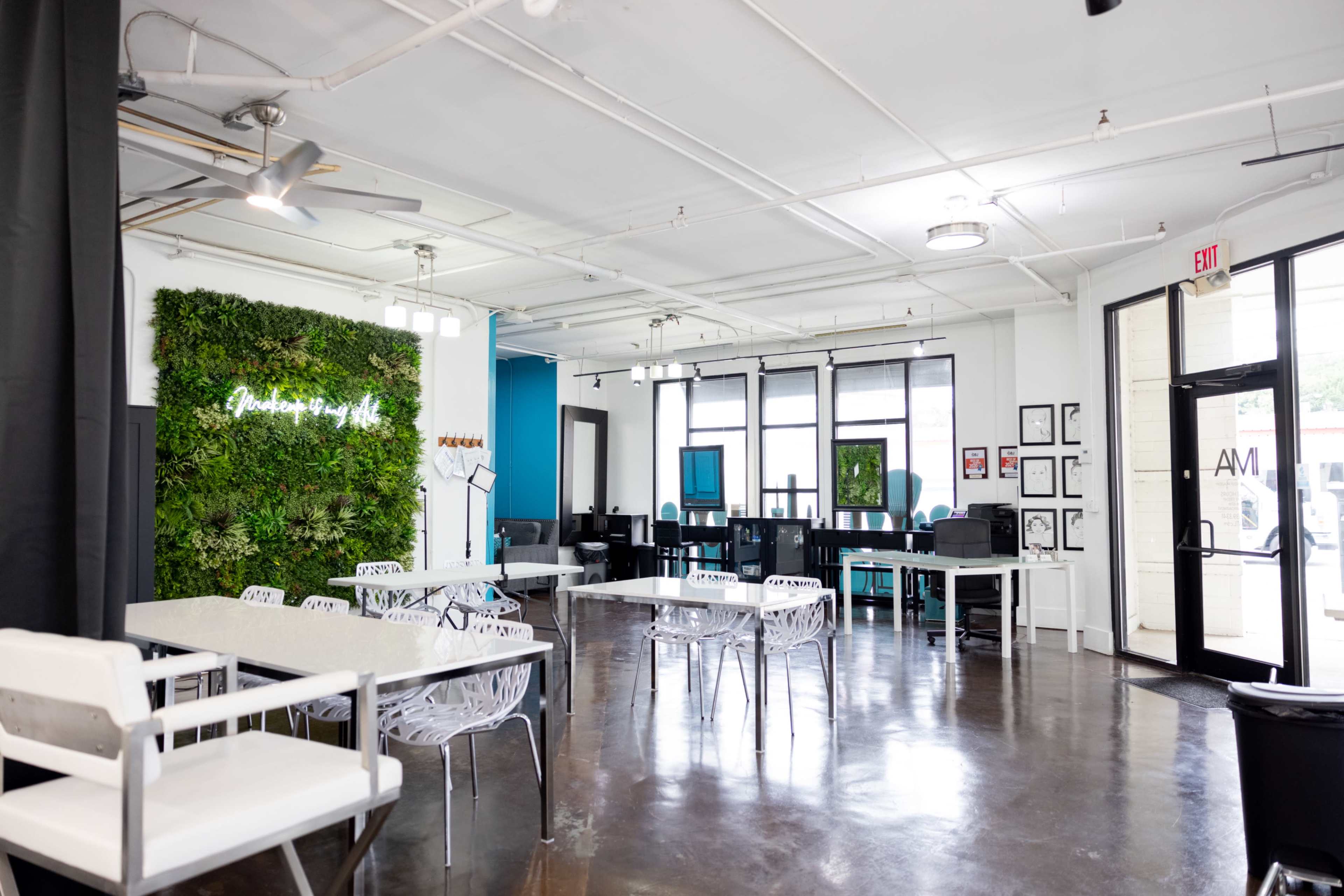 A modern, open workspace featuring a green wall, white furniture, and several workstations with computers.