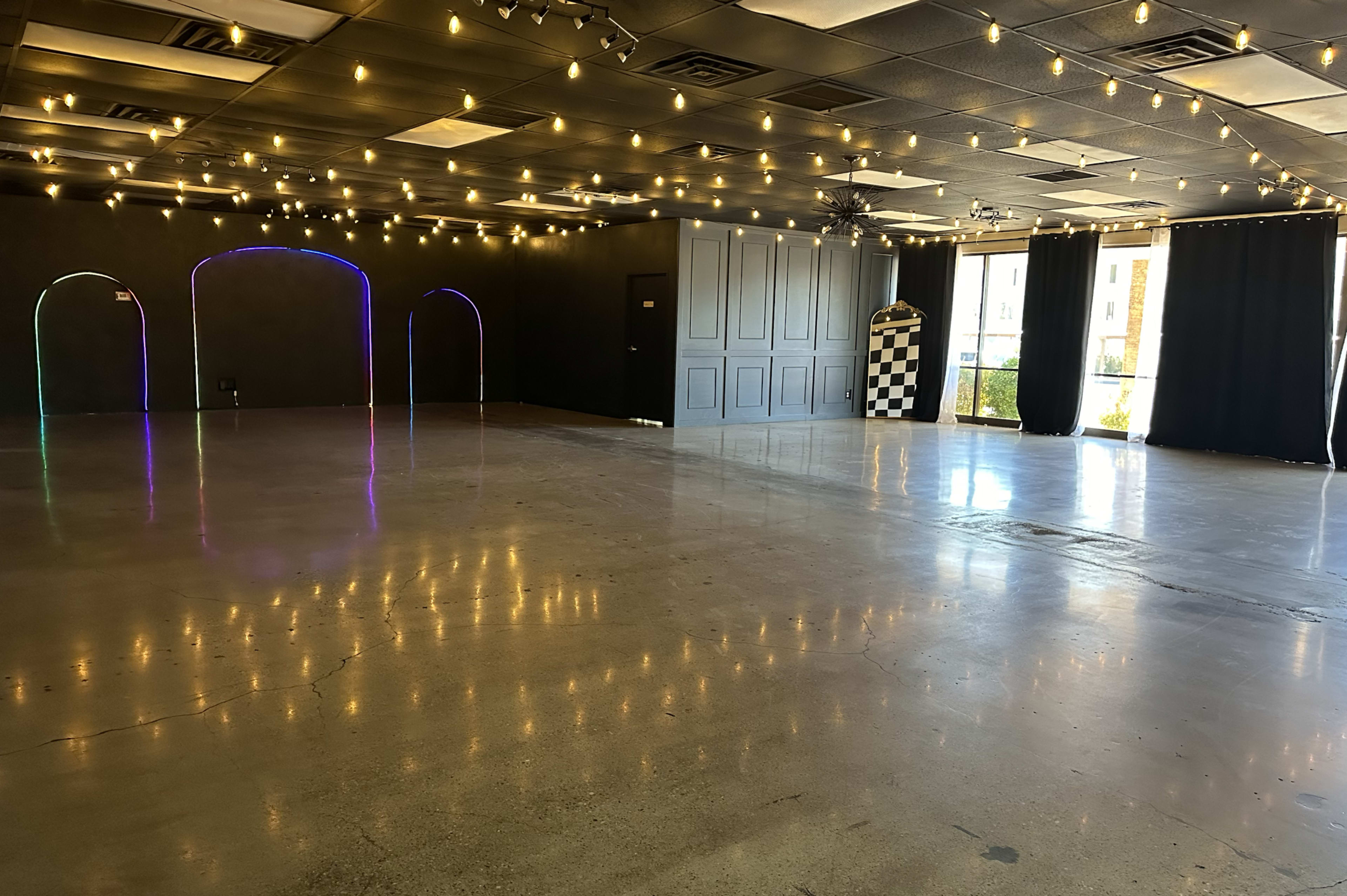 An empty event space with polished concrete floors, decorative string lights overhead, and colorful arches in the walls.