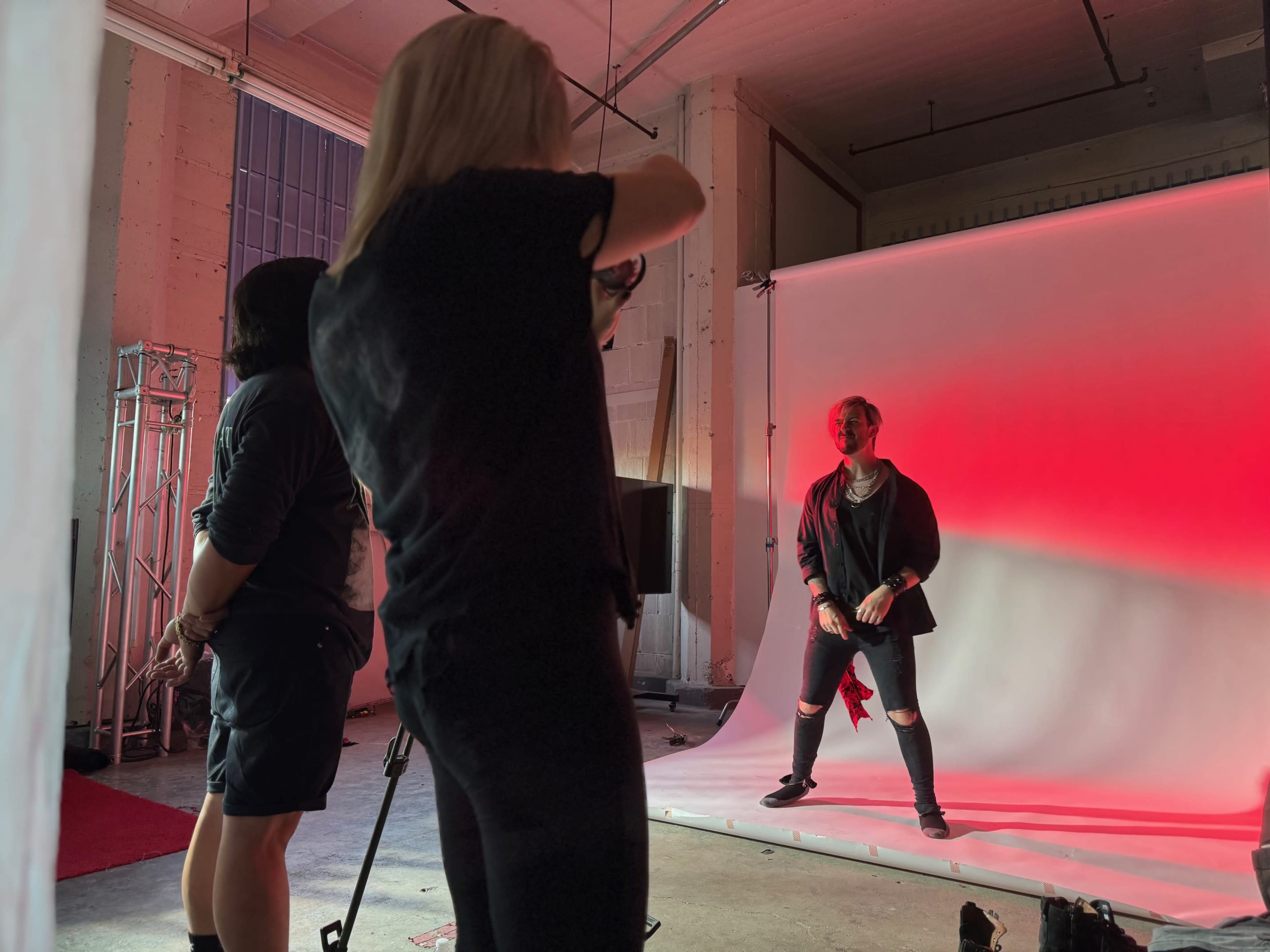 A photographer captures a model posing against a backdrop illuminated with red lighting in a studio setting.