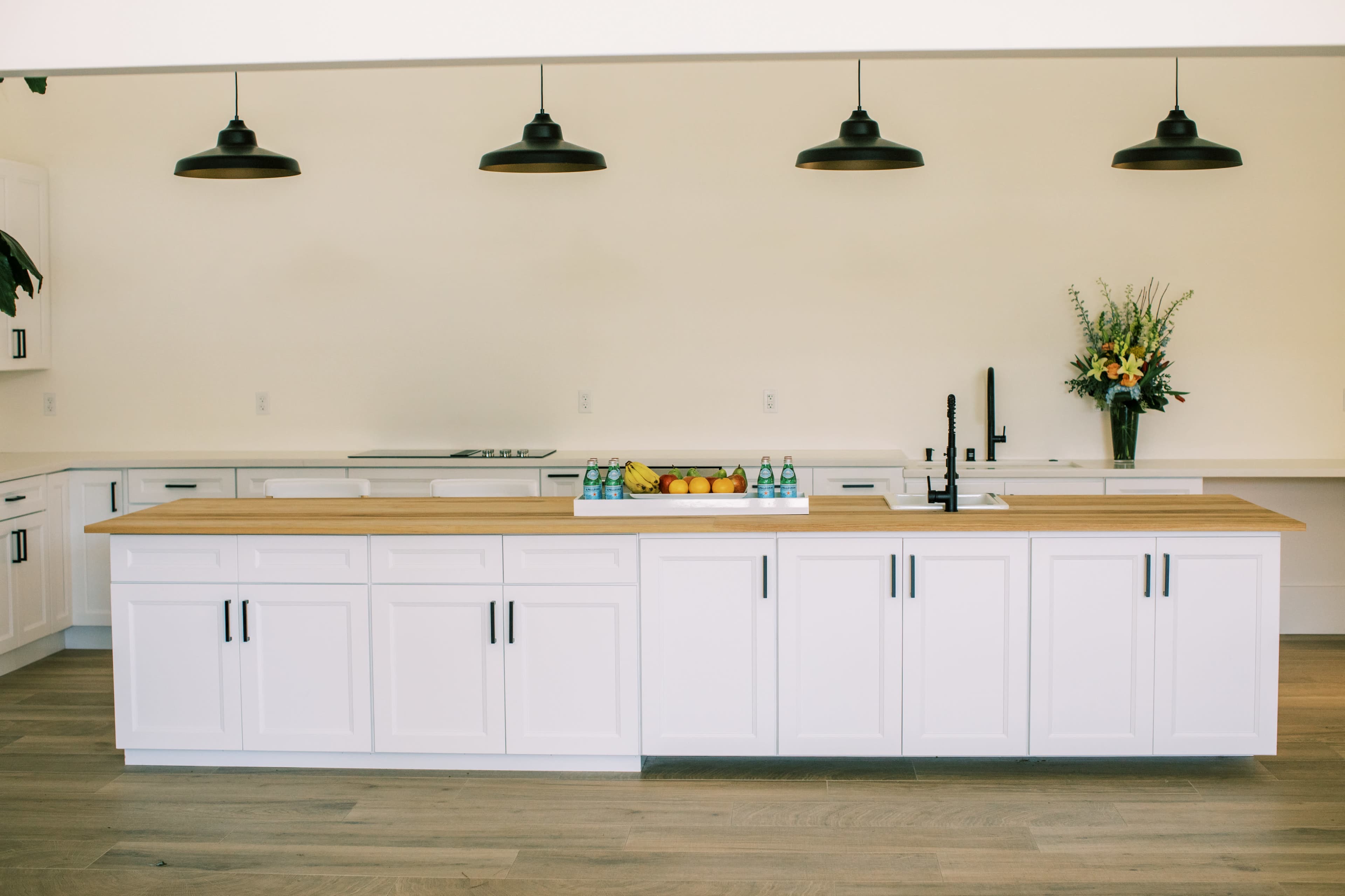 A modern kitchen with a central wooden island, white cabinetry, and three black pendant lights.