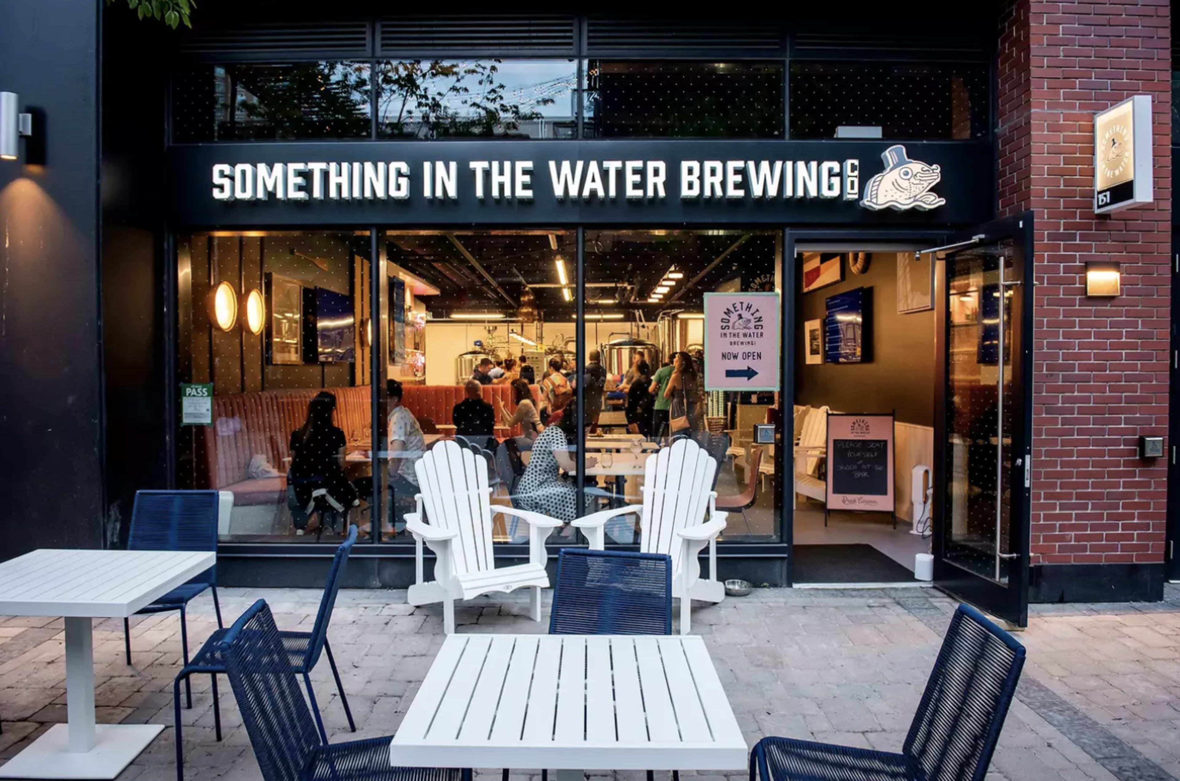 The exterior of "Something in the Water Brewing" features a welcoming entrance with outdoor seating and patrons visible inside.