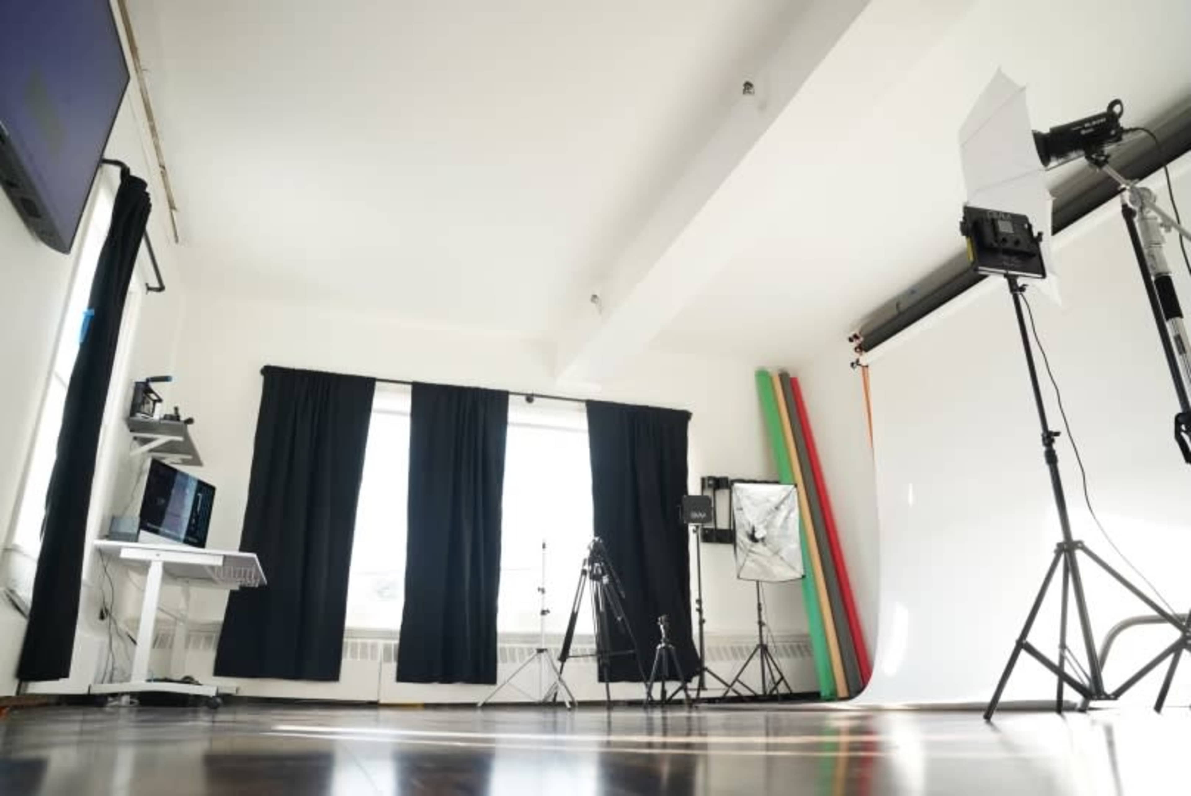 A photography studio is set up with equipment, including tripods, lights, a backdrop, and a computer workstation.
