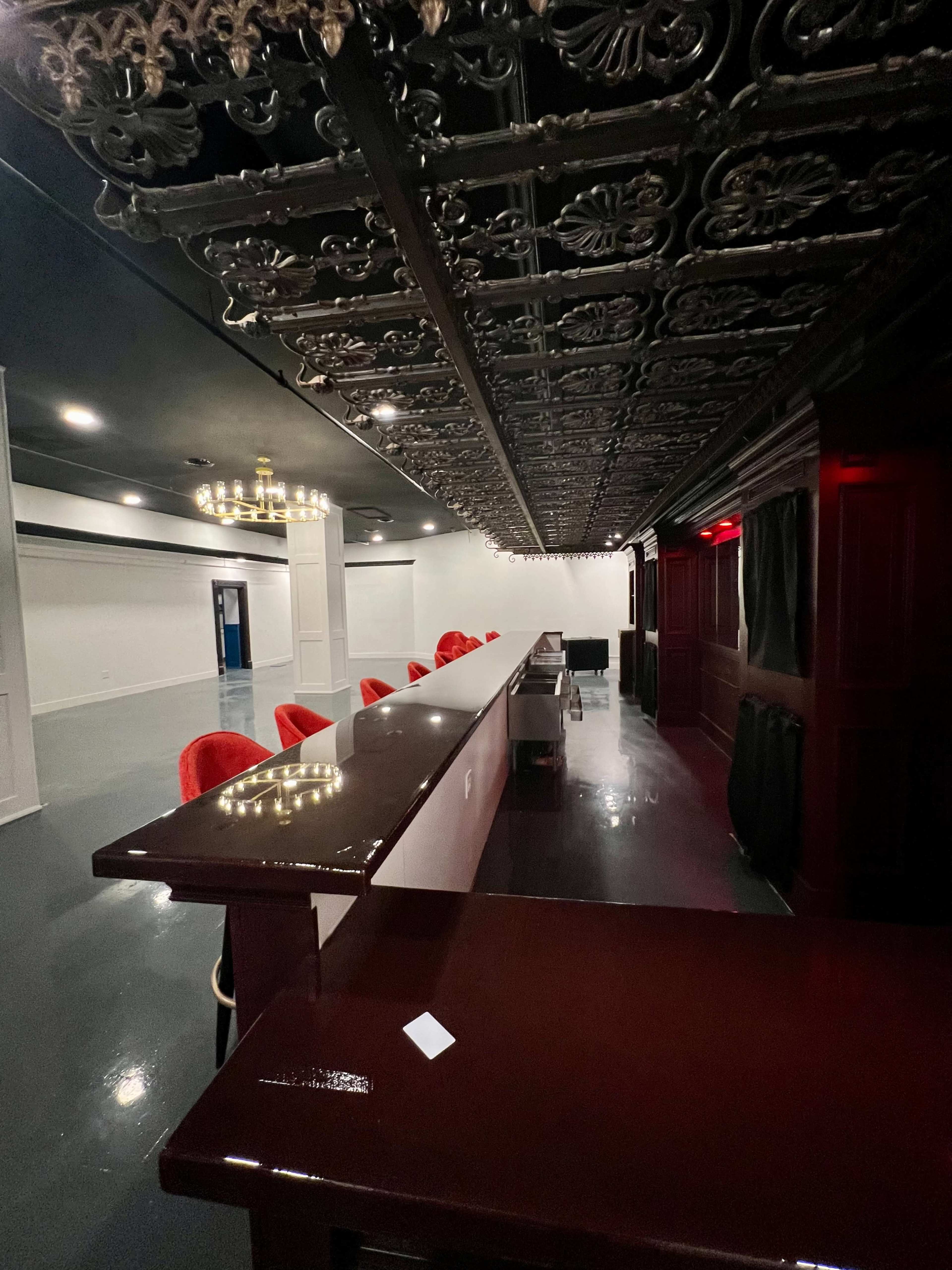 A spacious bar area with a long wooden counter, red upholstered chairs, and an ornate ceiling.
