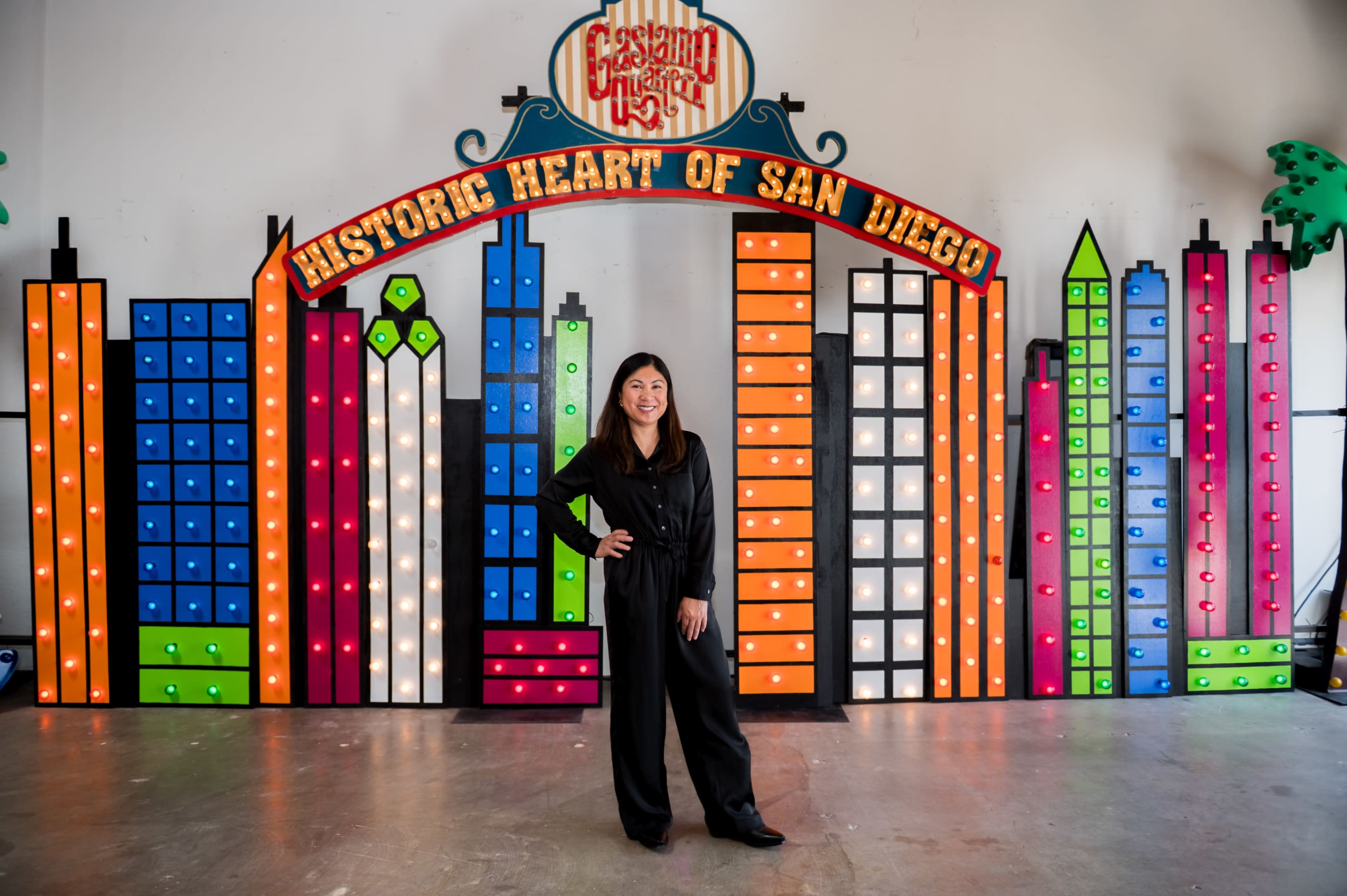 A person stands in front of a colorful, illuminated backdrop featuring a skyline design that represents San Diego.
