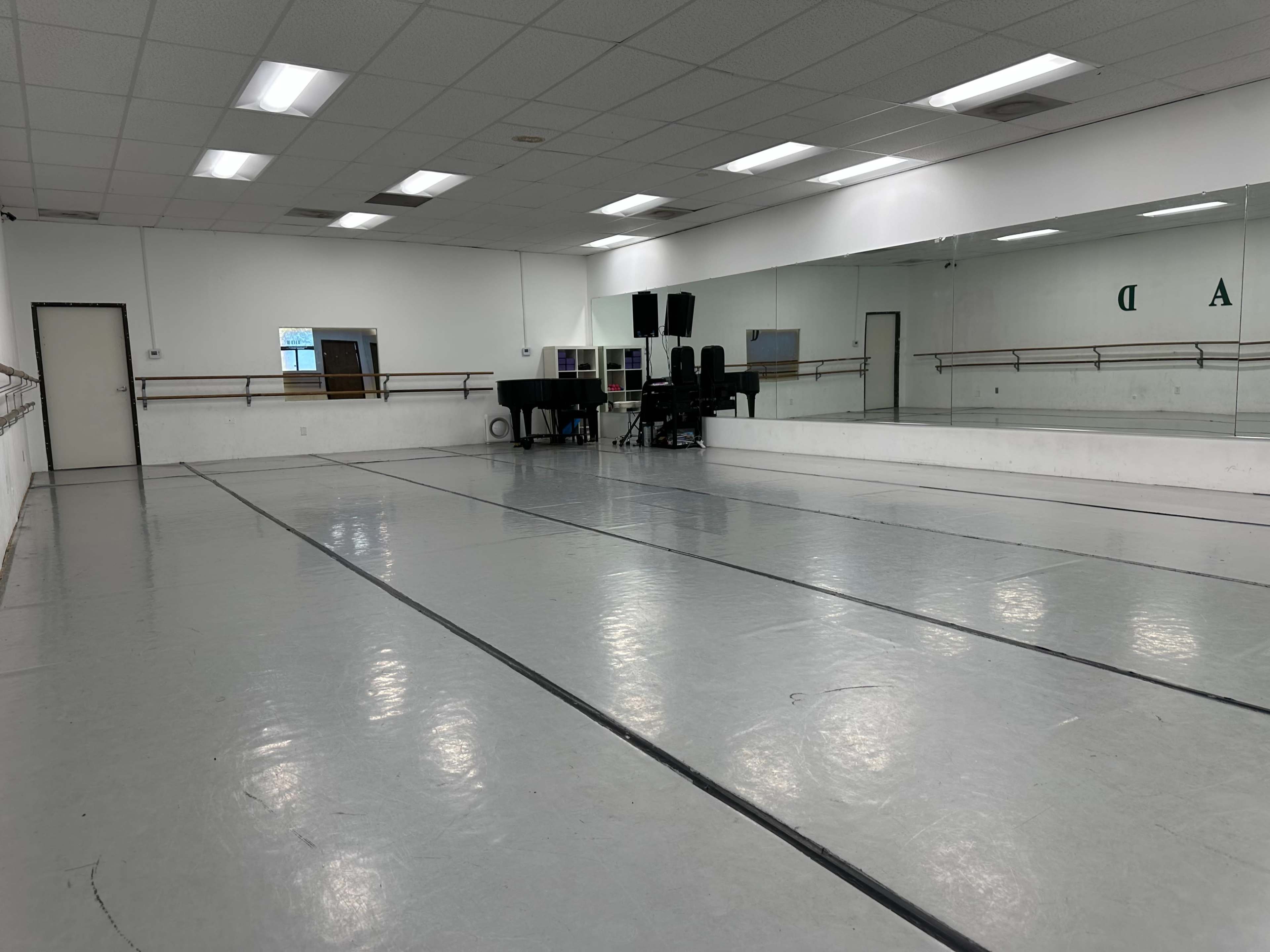 The image shows an empty dance studio with a mirrored wall and ballet barres along one side.