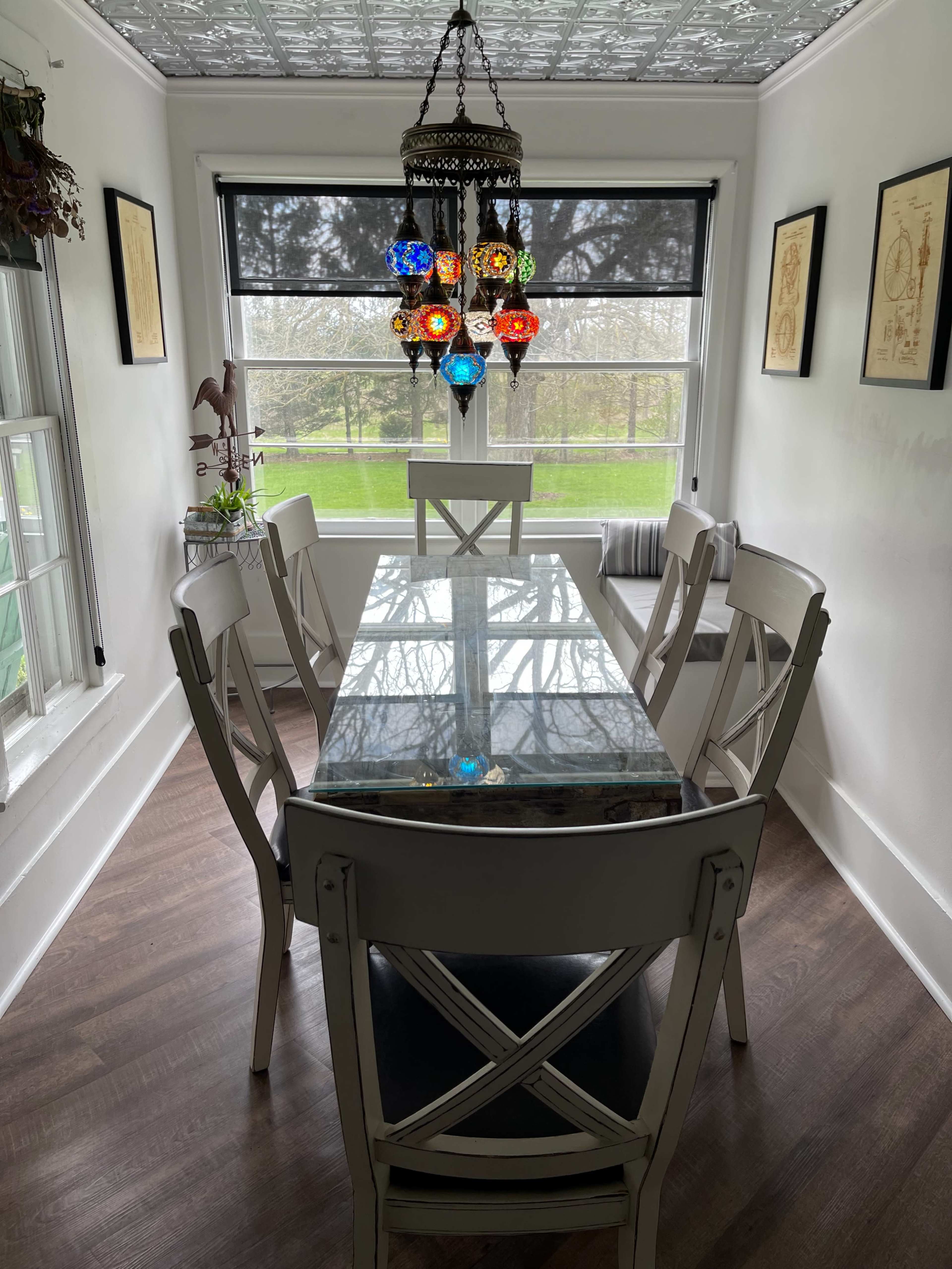 A rectangular dining table with a glass top is surrounded by six chairs under a colorful chandelier in a well-lit dining area.