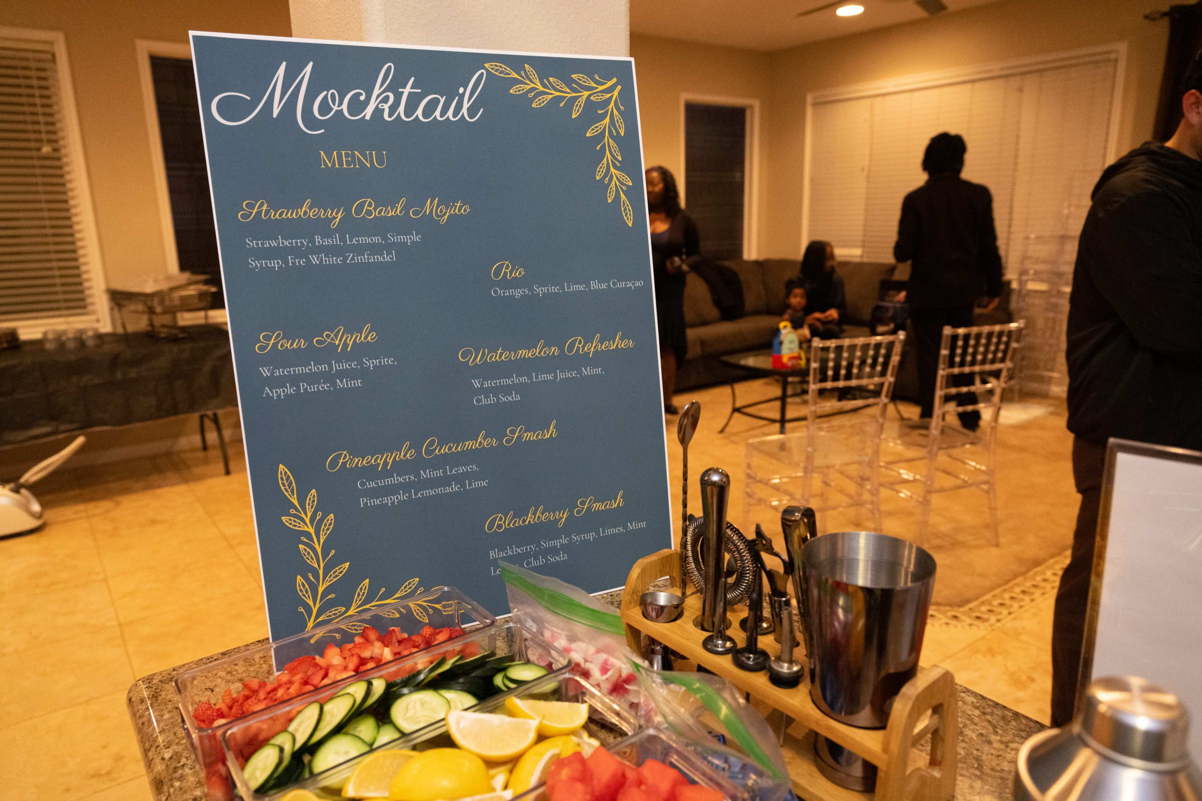 A mocktail menu displayed on a blue board lists various drink options alongside a preparation station featuring fresh fruits and garnishes.