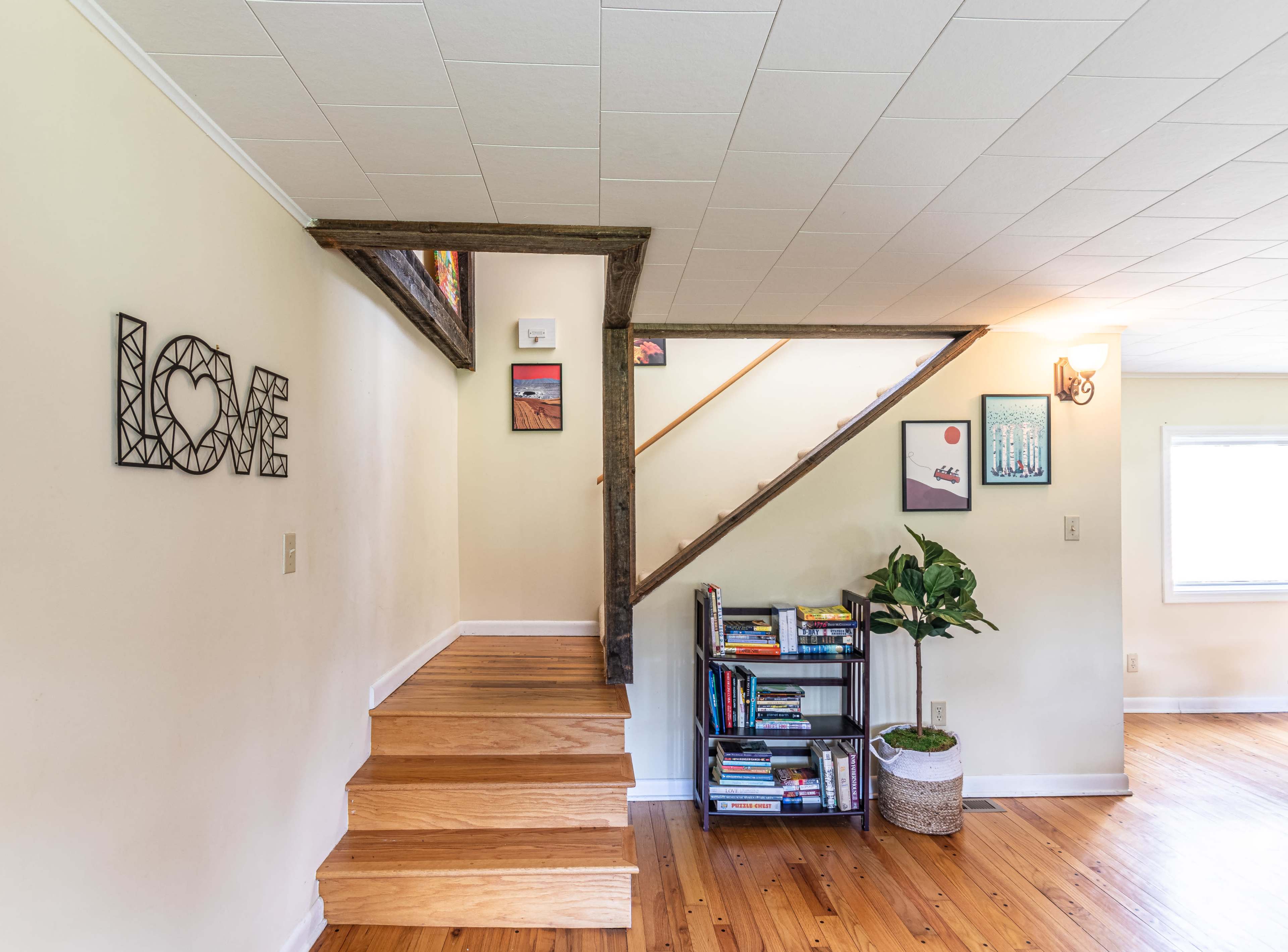 A stairway leading to an upper level, with a decorative "LOVE" sign on the wall and a bookshelf filled with books beside a plant.