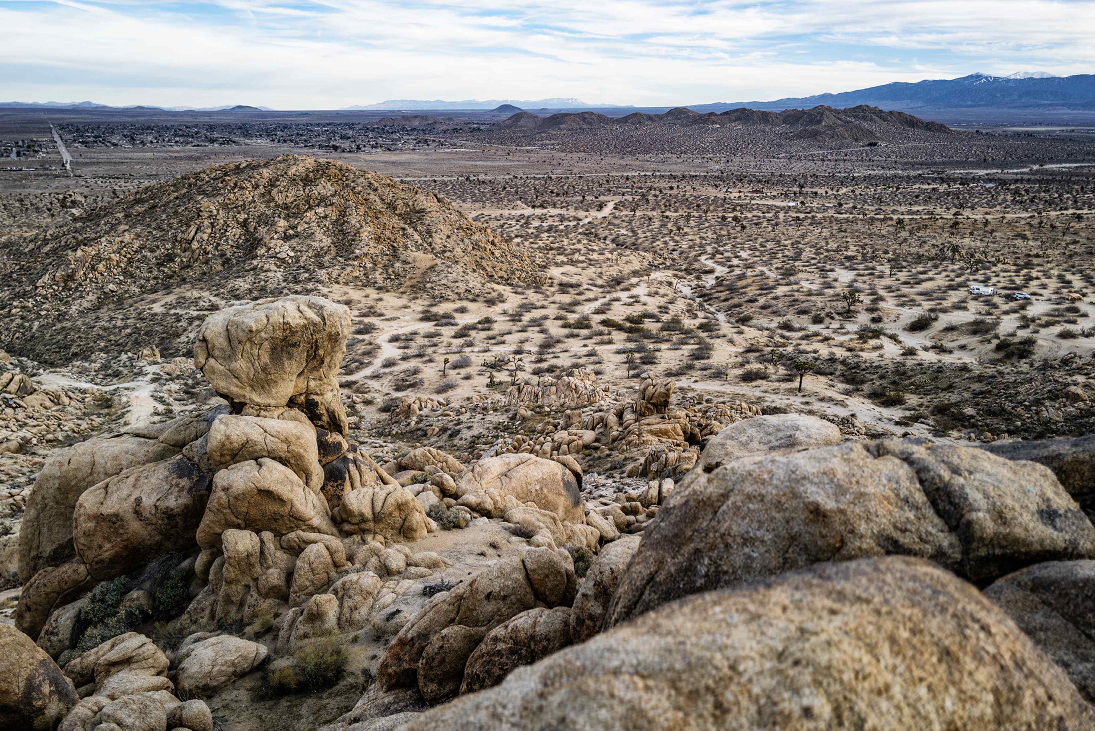A rocky landscape of desert terrain, featuring large boulders and sparse vegetation under a cloudy sky.