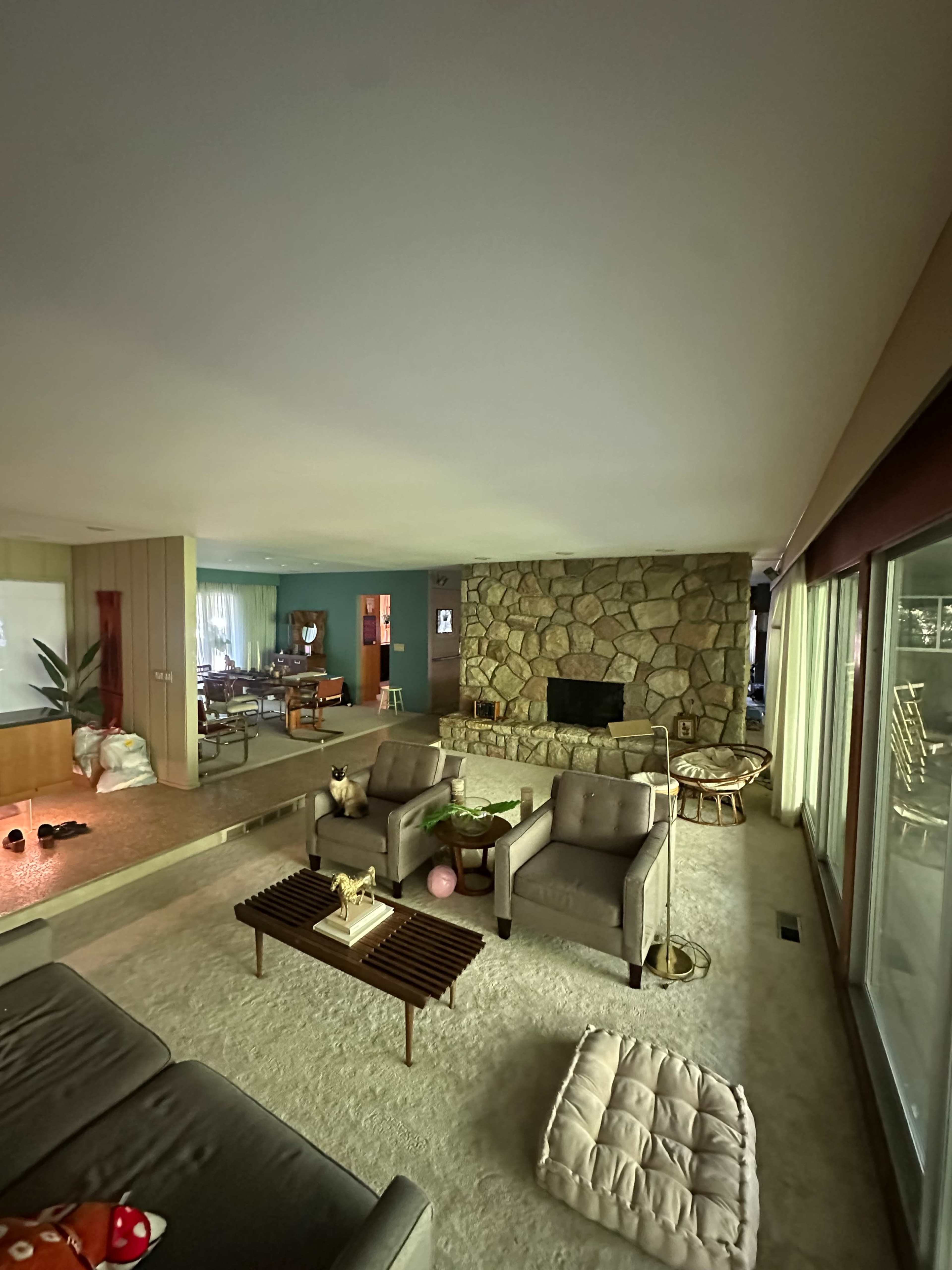 A spacious living room features a stone fireplace, two armchairs, a sectional sofa, and large windows letting in natural light.