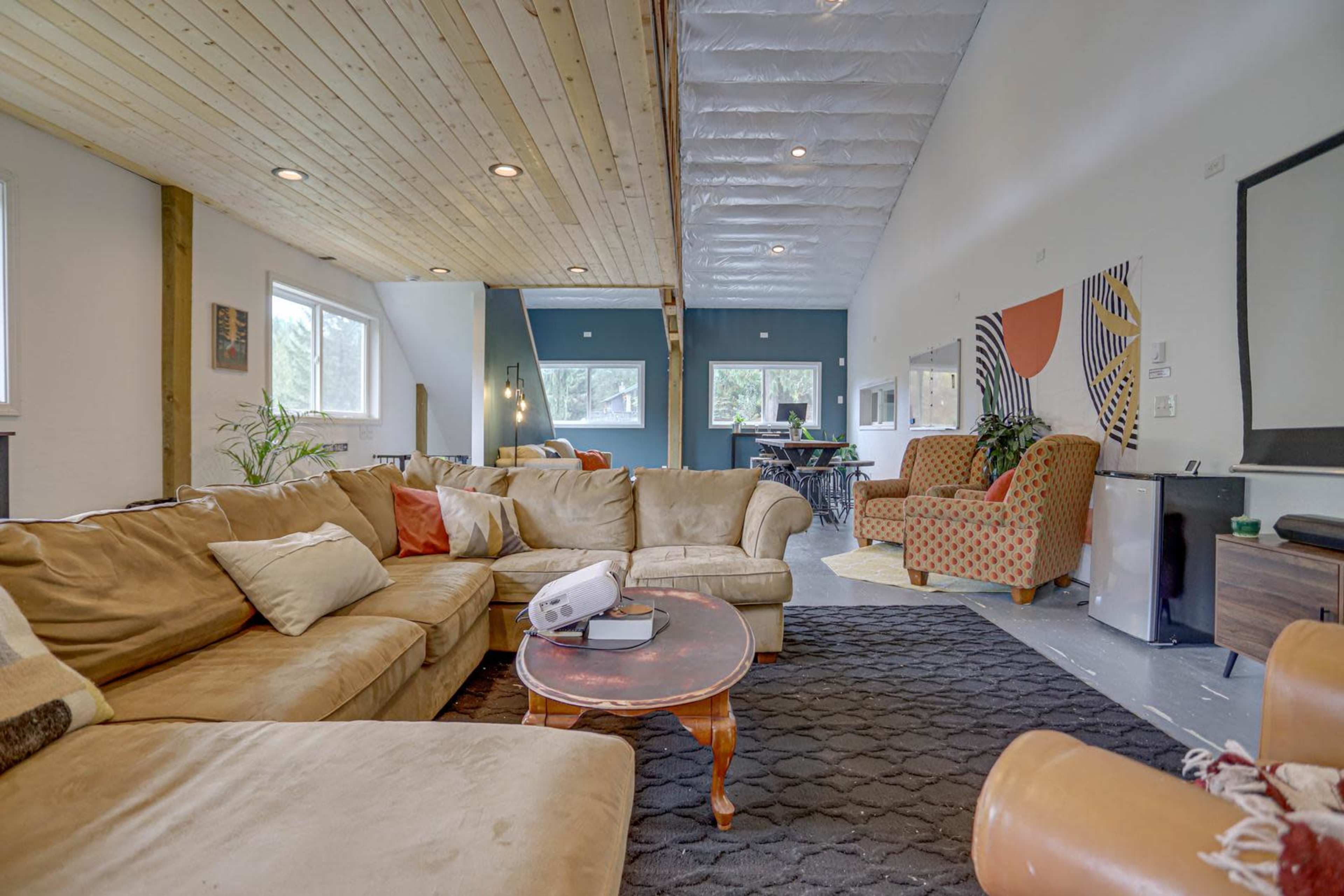 A spacious living room features a large sectional sofa, a coffee table, and various seating arrangements under a wooden ceiling.