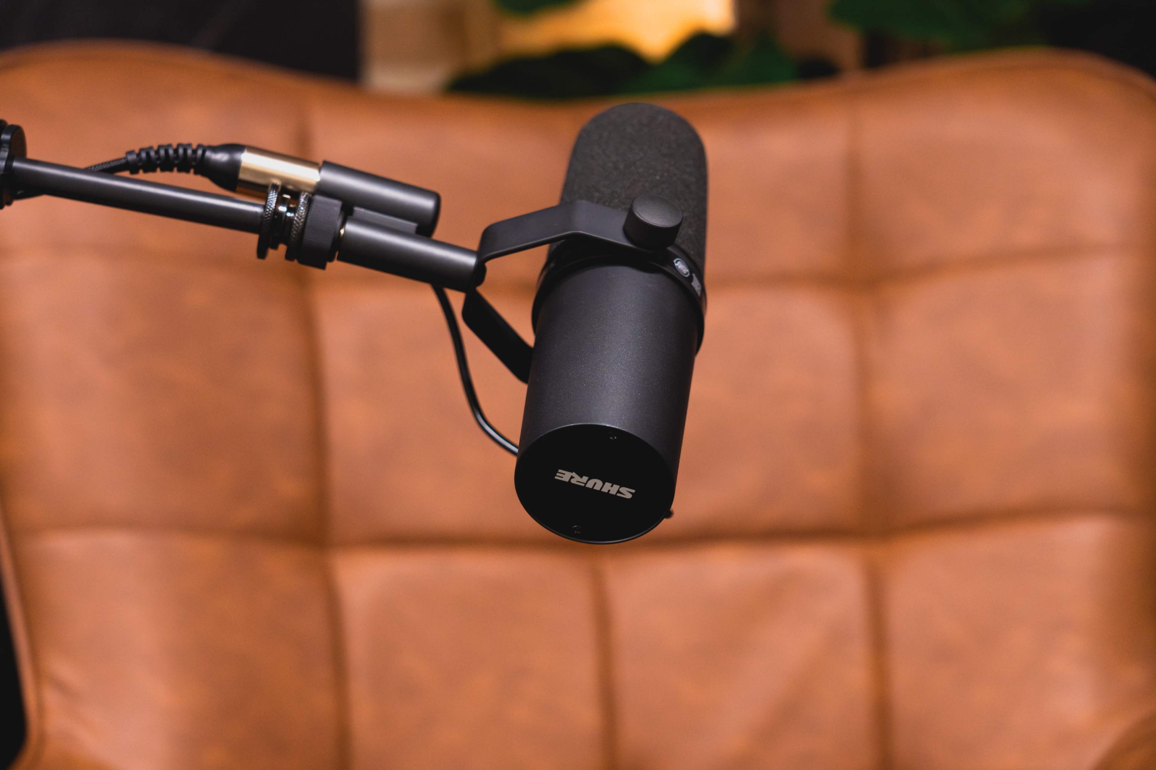 A black microphone is mounted on a boom arm in front of a brown leather couch.