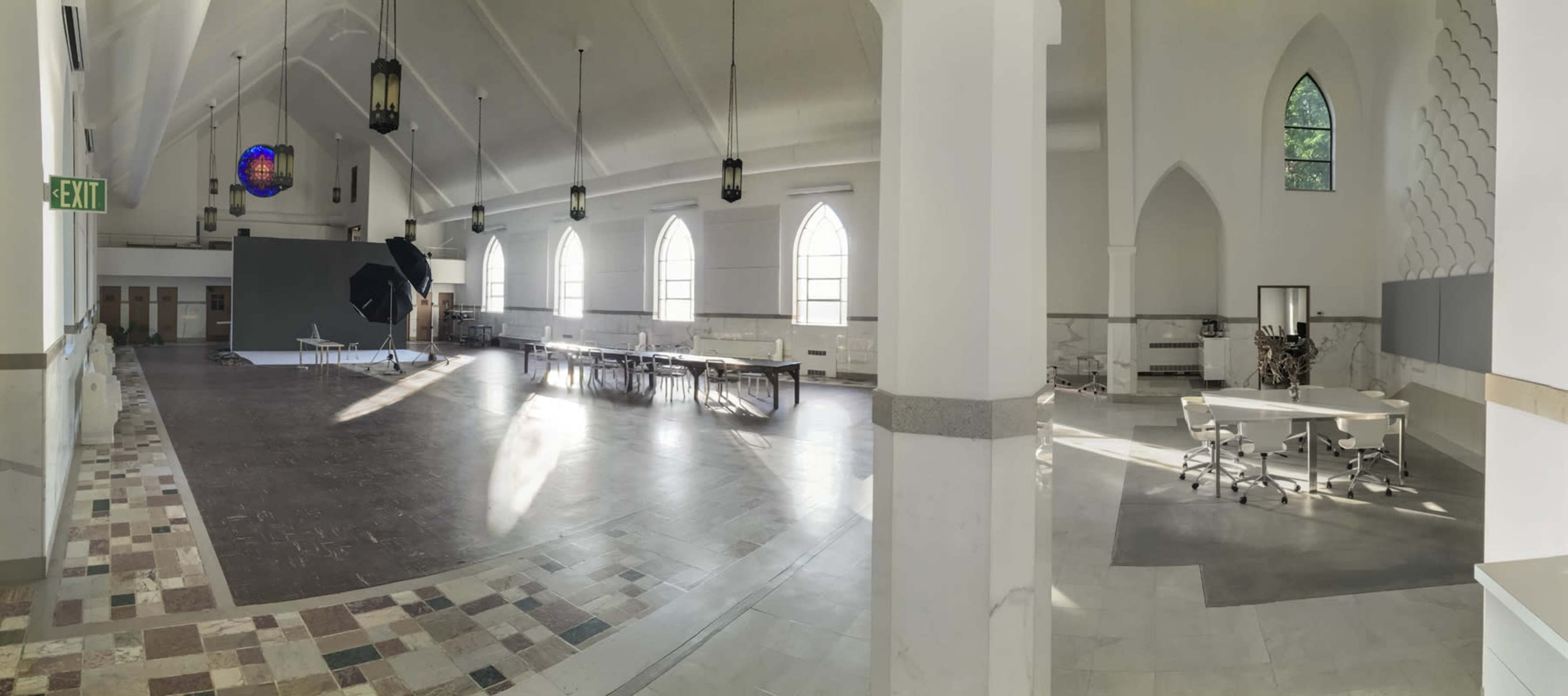 A spacious, well-lit interior of a converted church, featuring wooden tables, chairs, and a photography setup in a corner.