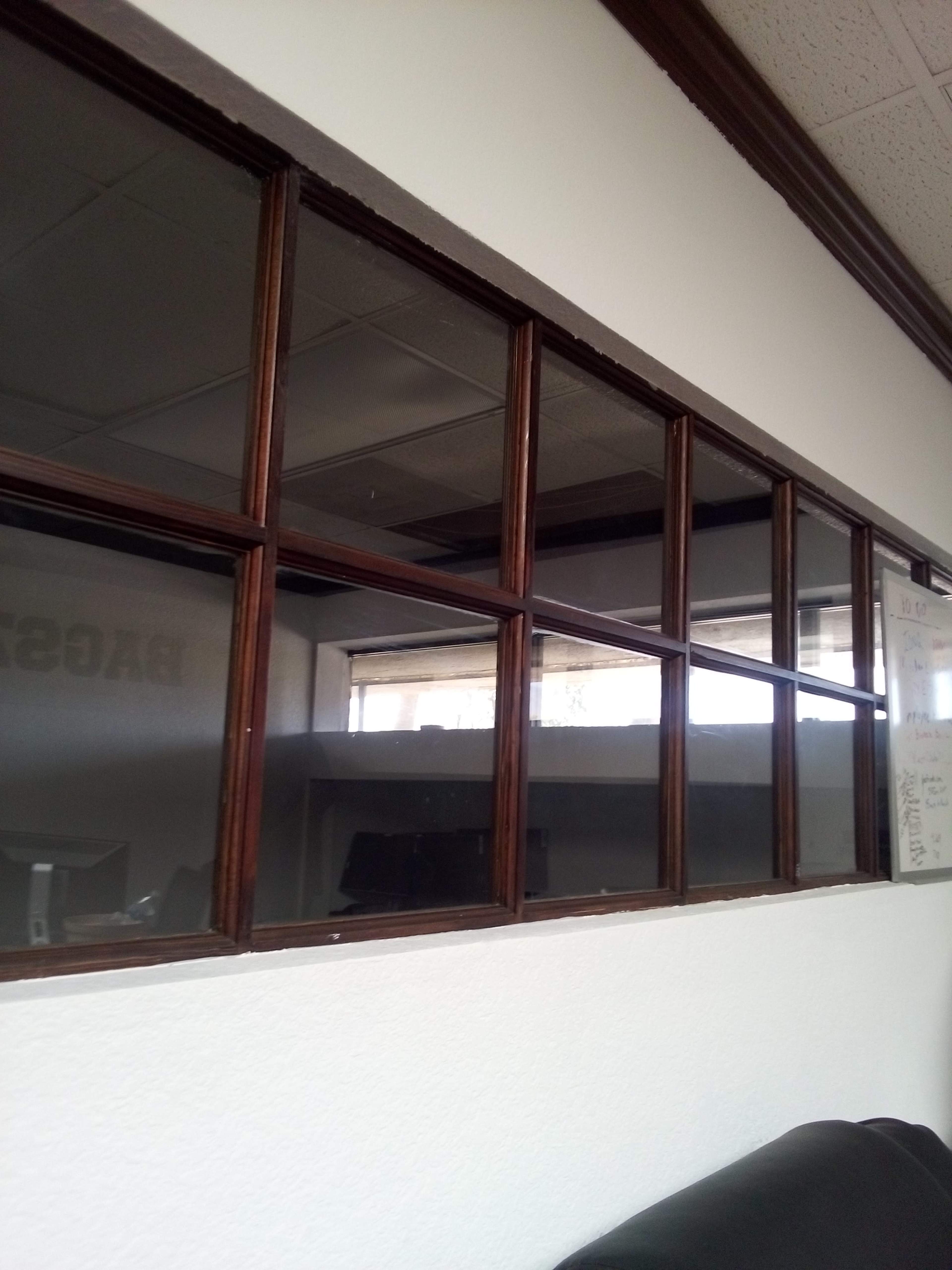 A series of wooden-framed windows set in a white wall, with a view of an office space beyond.