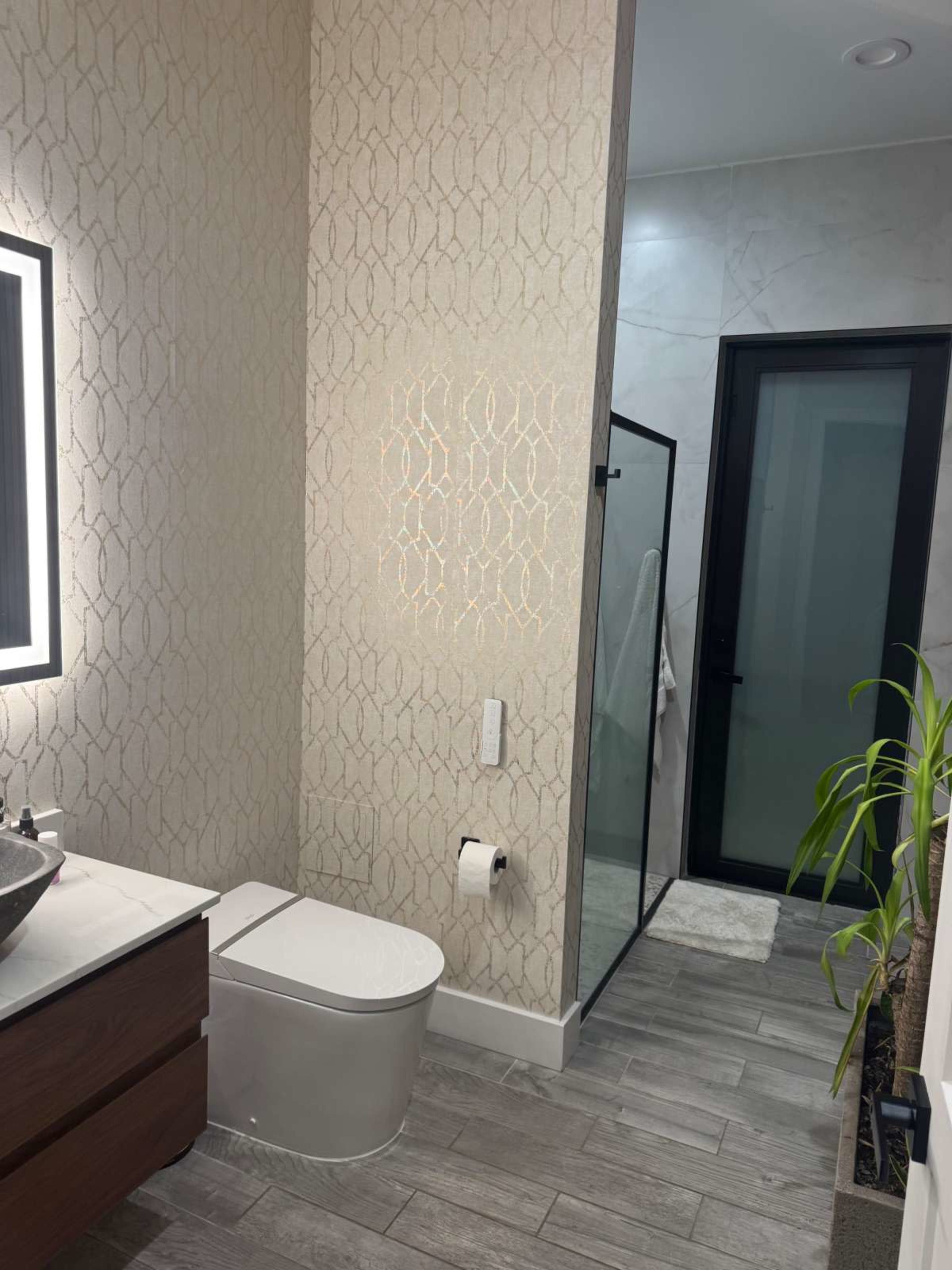 The image shows a modern bathroom featuring a toilet, a vanity with a sink, and a glass shower enclosure.