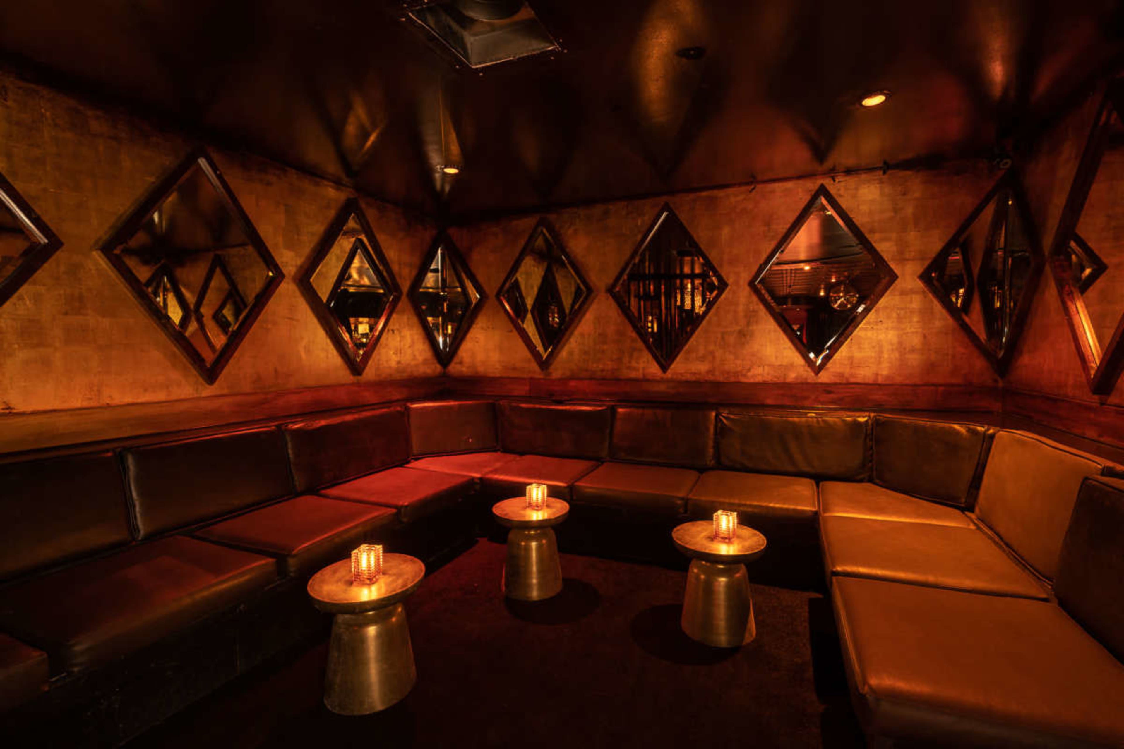 The image shows a dimly lit lounge with a curved leather seating area and small round tables topped with candles.