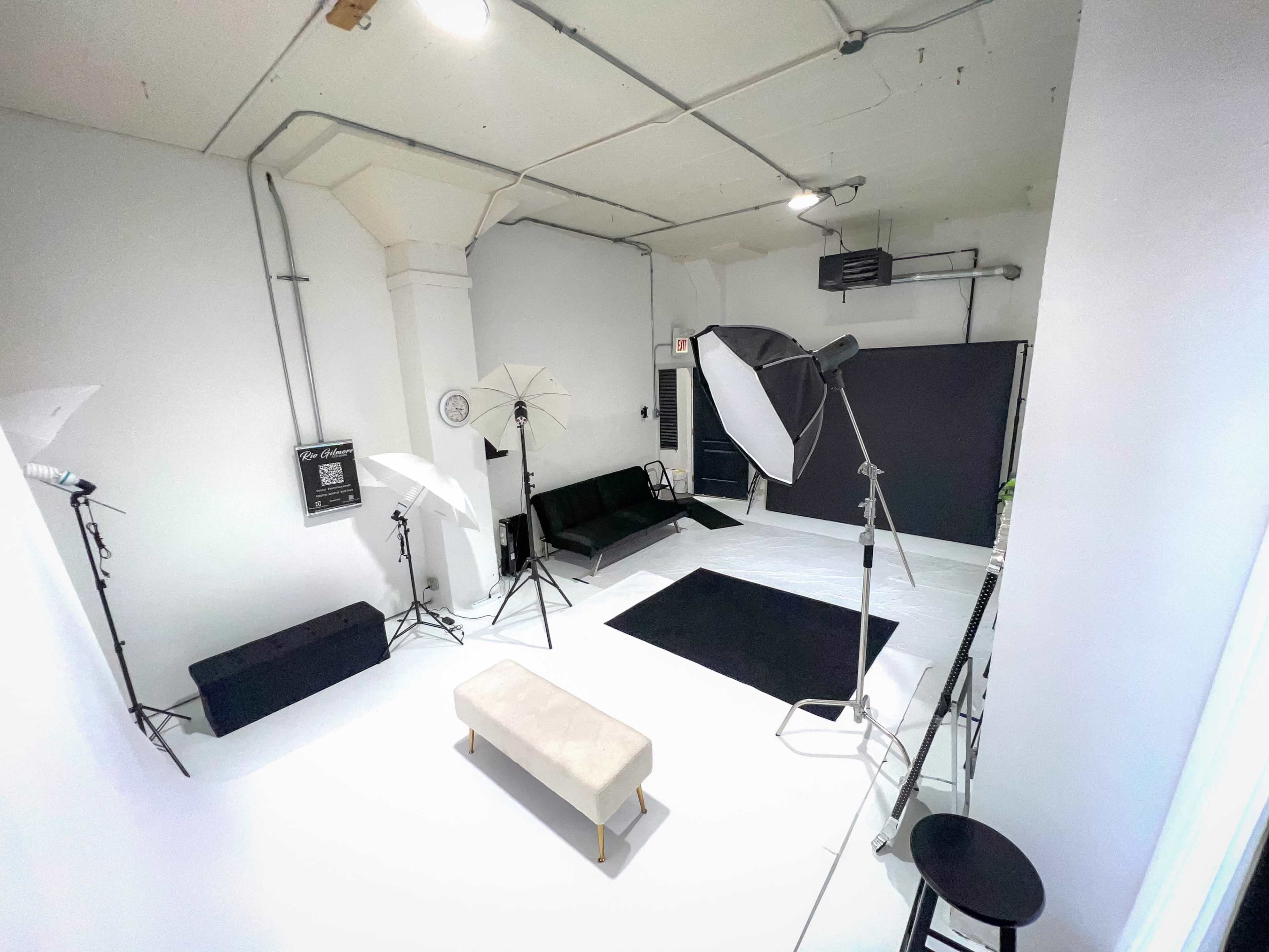 The image shows a photography studio with a black couch, black backdrop, and multiple lighting setups.