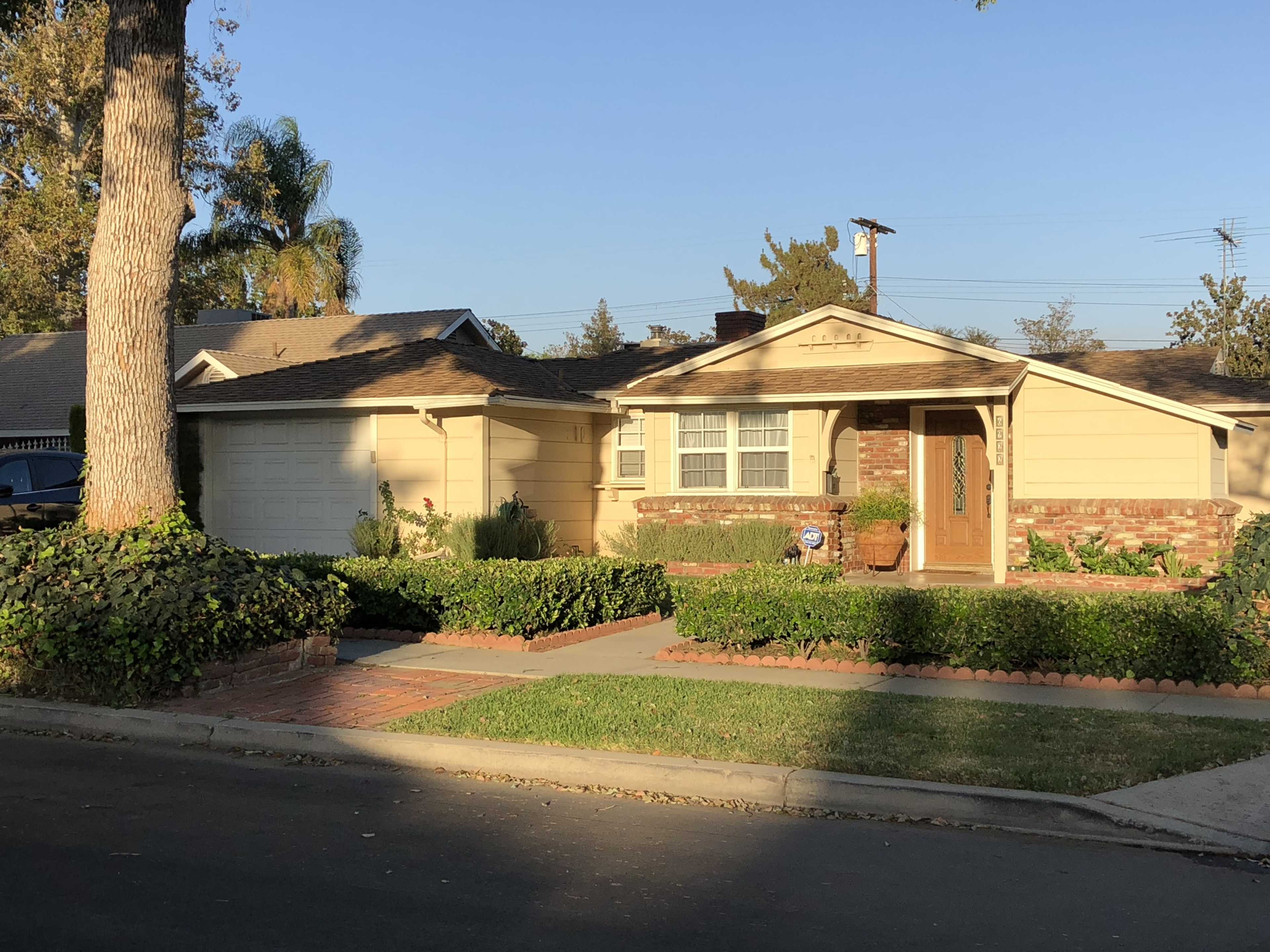 A single-story house with a brick porch, well-maintained landscaping, and a driveway, under a clear blue sky.