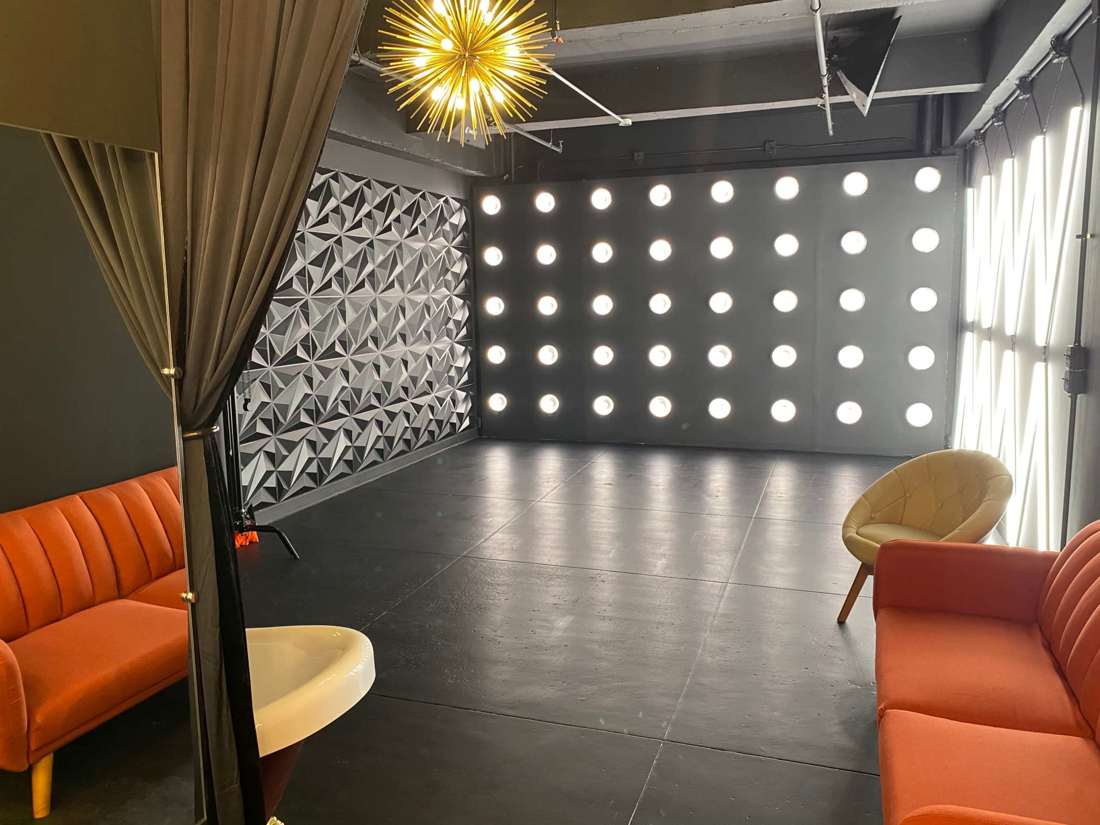A modern studio space with a geometric wall design, bright lighting, and two orange sofas.