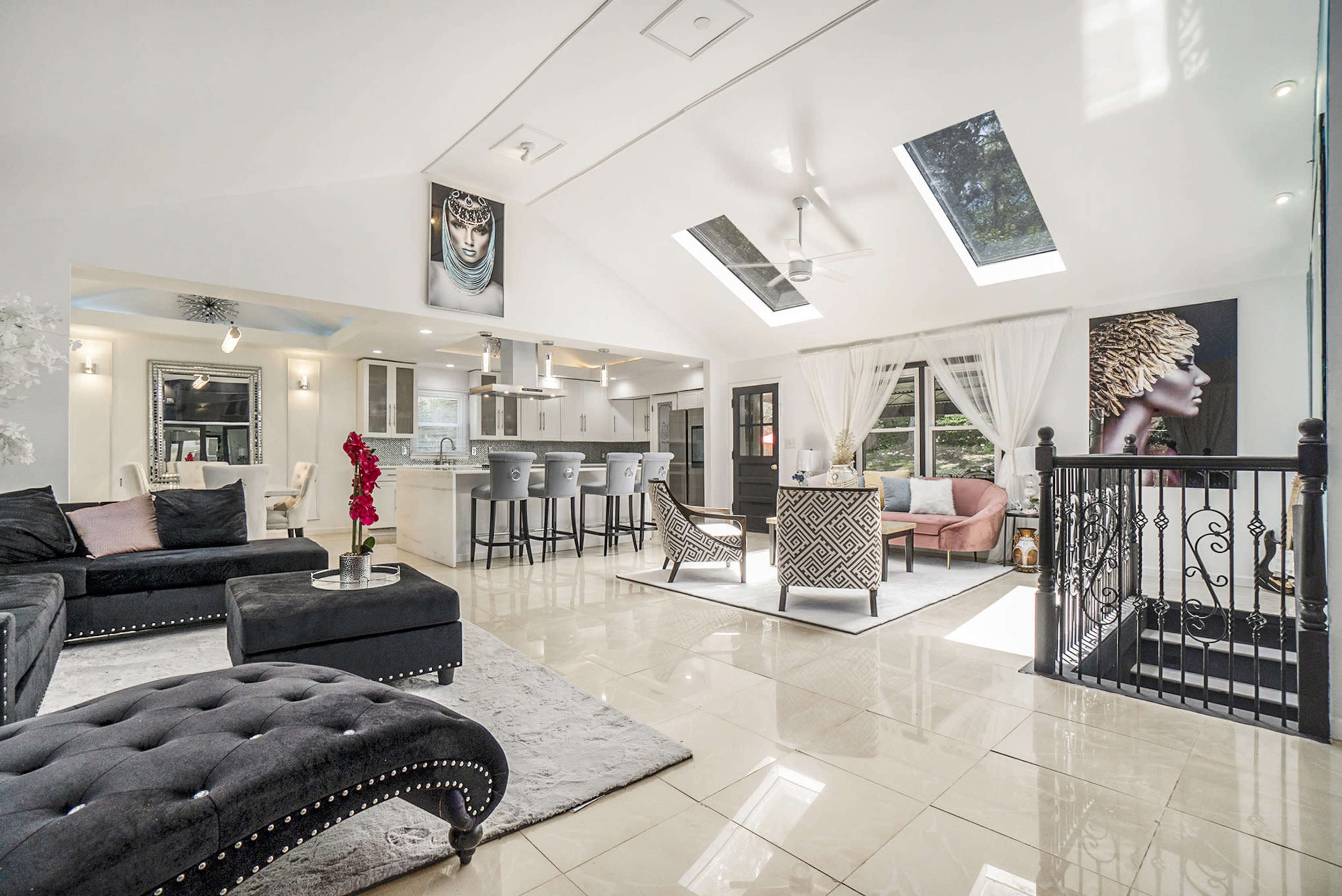 A modern living area with large windows, a stylish kitchen, and elegant furniture including a black sectional sofa and decorative artwork on the walls.